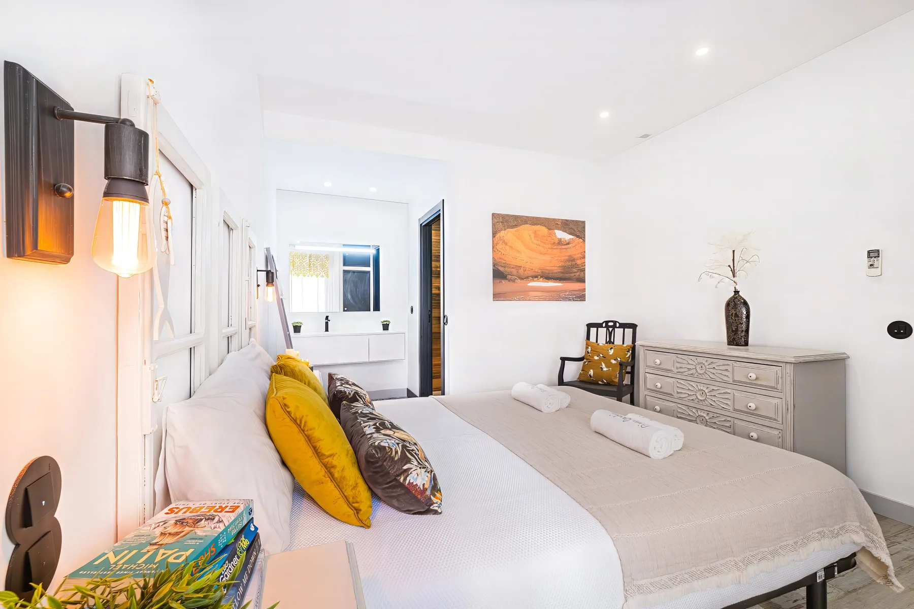A bright bedroom with a bed, mustard-colored pillows, and a dresser.