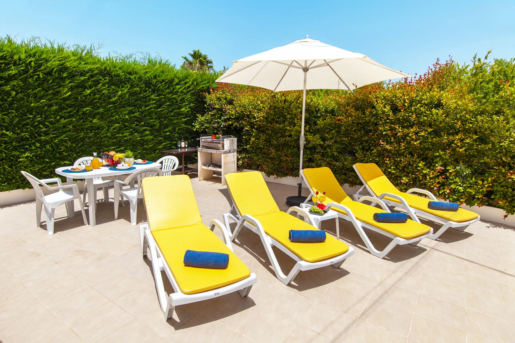 A sunny patio with yellow loungers, a dining table, and a large umbrella.