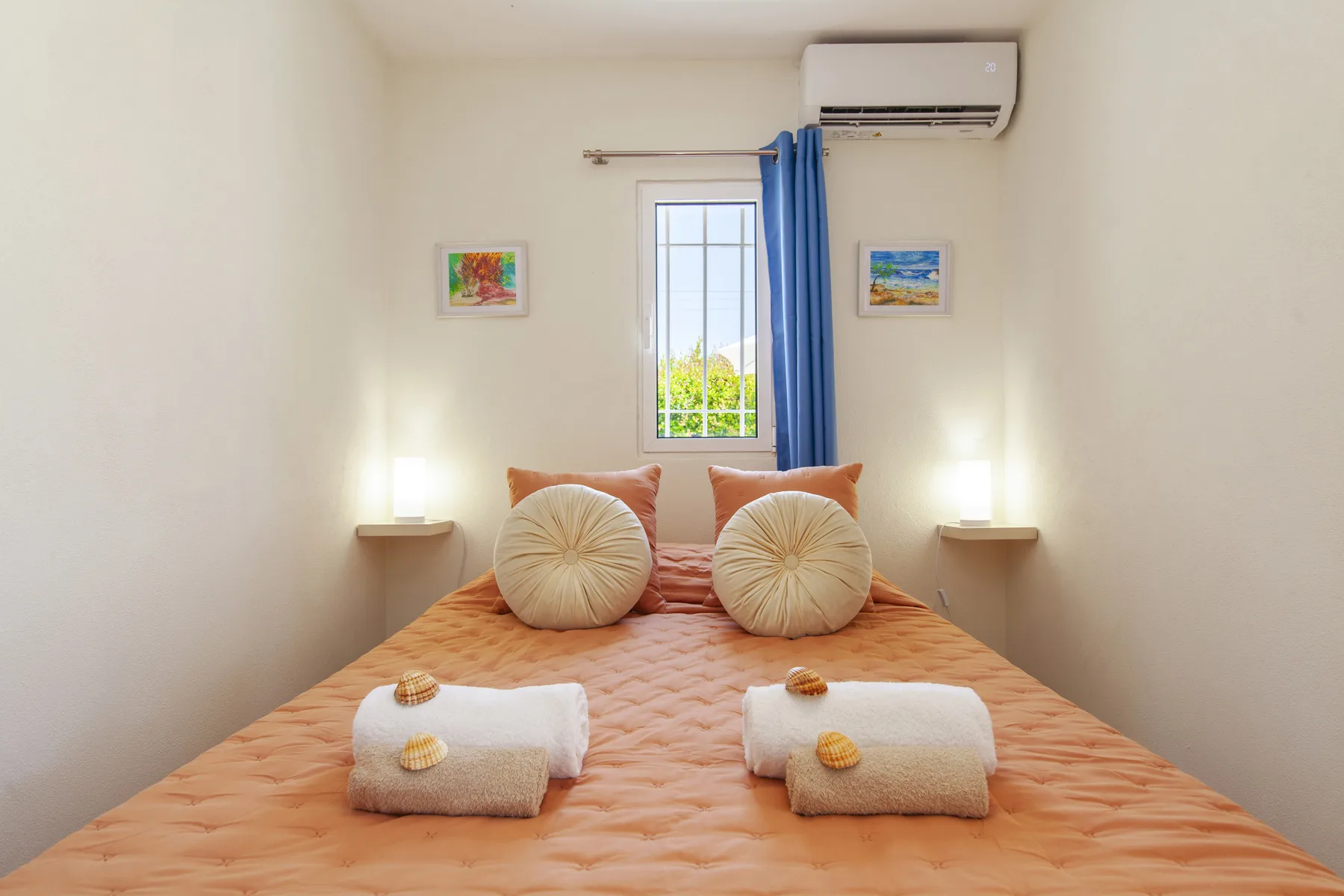 A bedroom with a bed dressed in peach bedding beneath a window with blue curtains.
