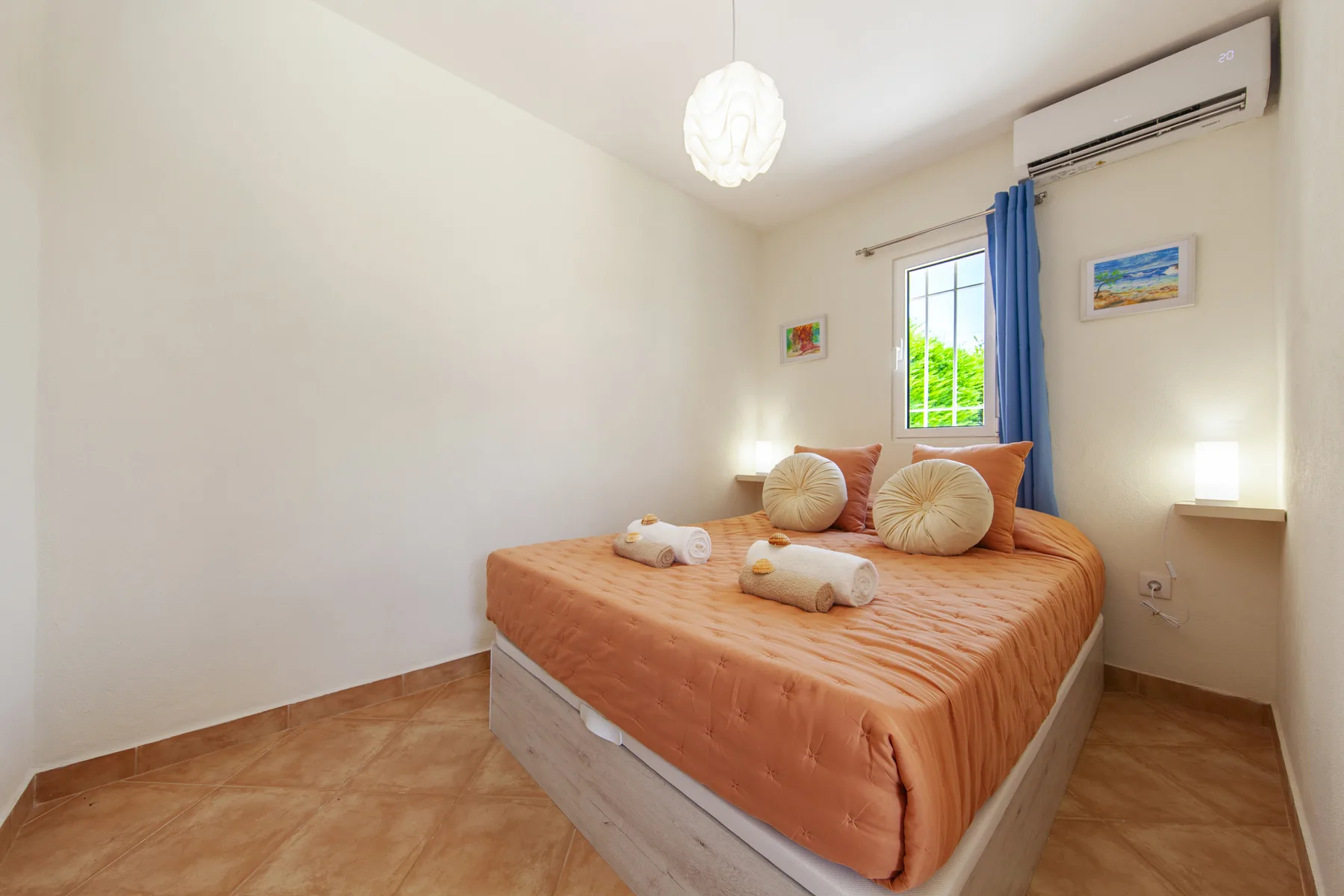 A bedroom with an orange bed, decorative pillows, and a window with blue curtains.