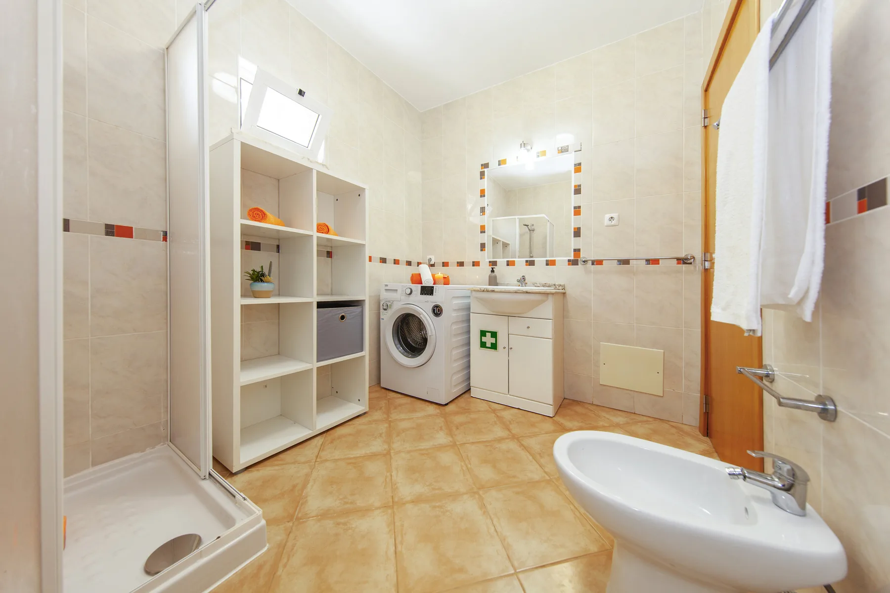 A tiled bathroom with a shower, washing machine, sink, and bidet.