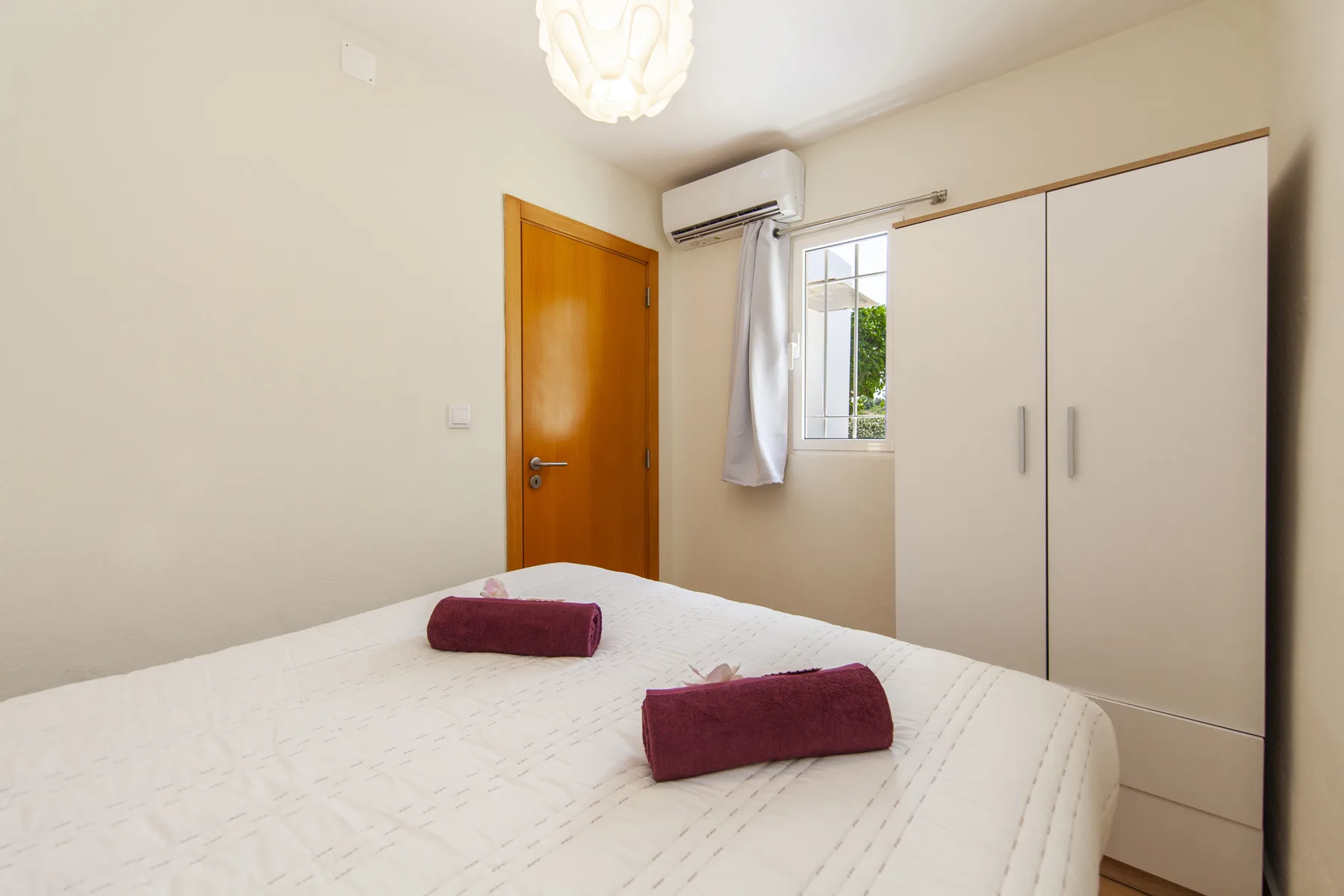 A bedroom with a bed, wardrobe, and window beside the door.