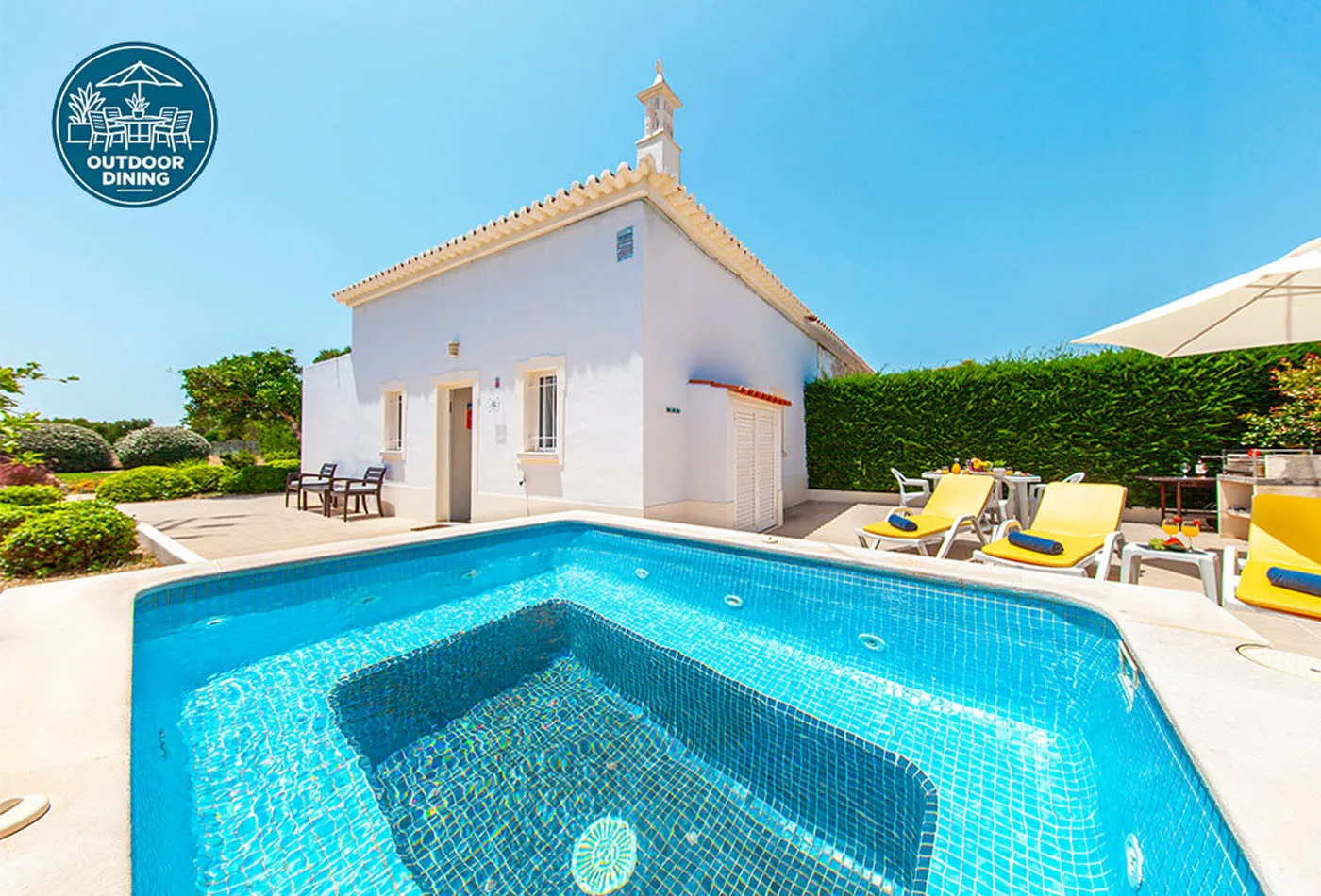 An outdoor swimming pool sits beside a small white building and patio seating.