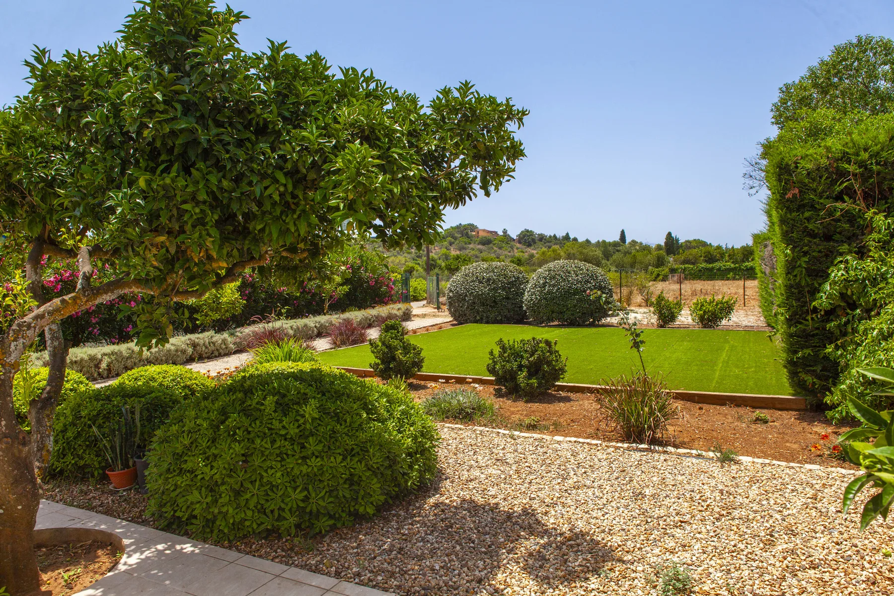 A landscaped garden with gravel paths, trimmed shrubs, and a green lawn.
