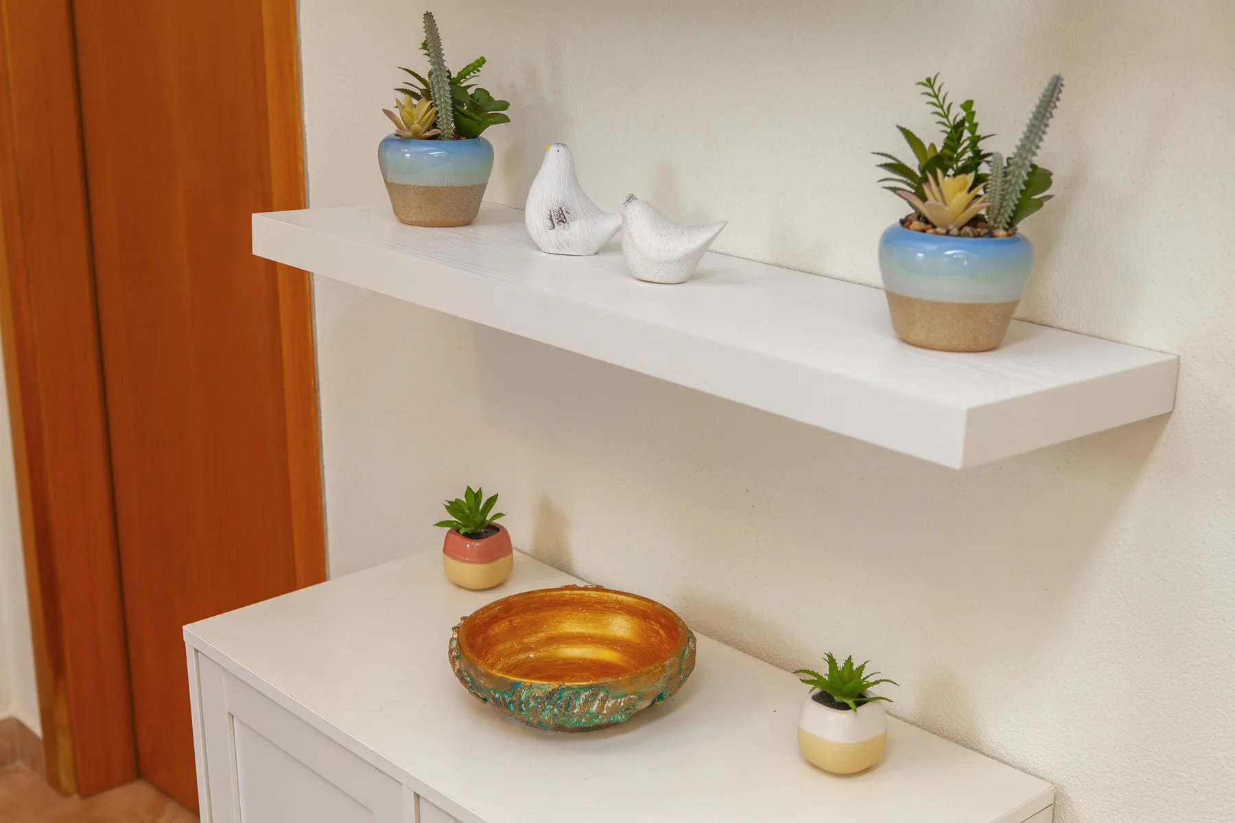 A white display shelf and cabinet hold small potted plants and decorative ceramics.