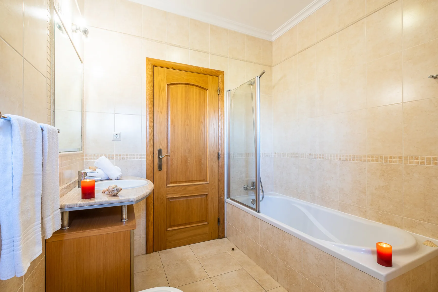Un baño alicatado con una puerta de madera, lavabo y bañera.
