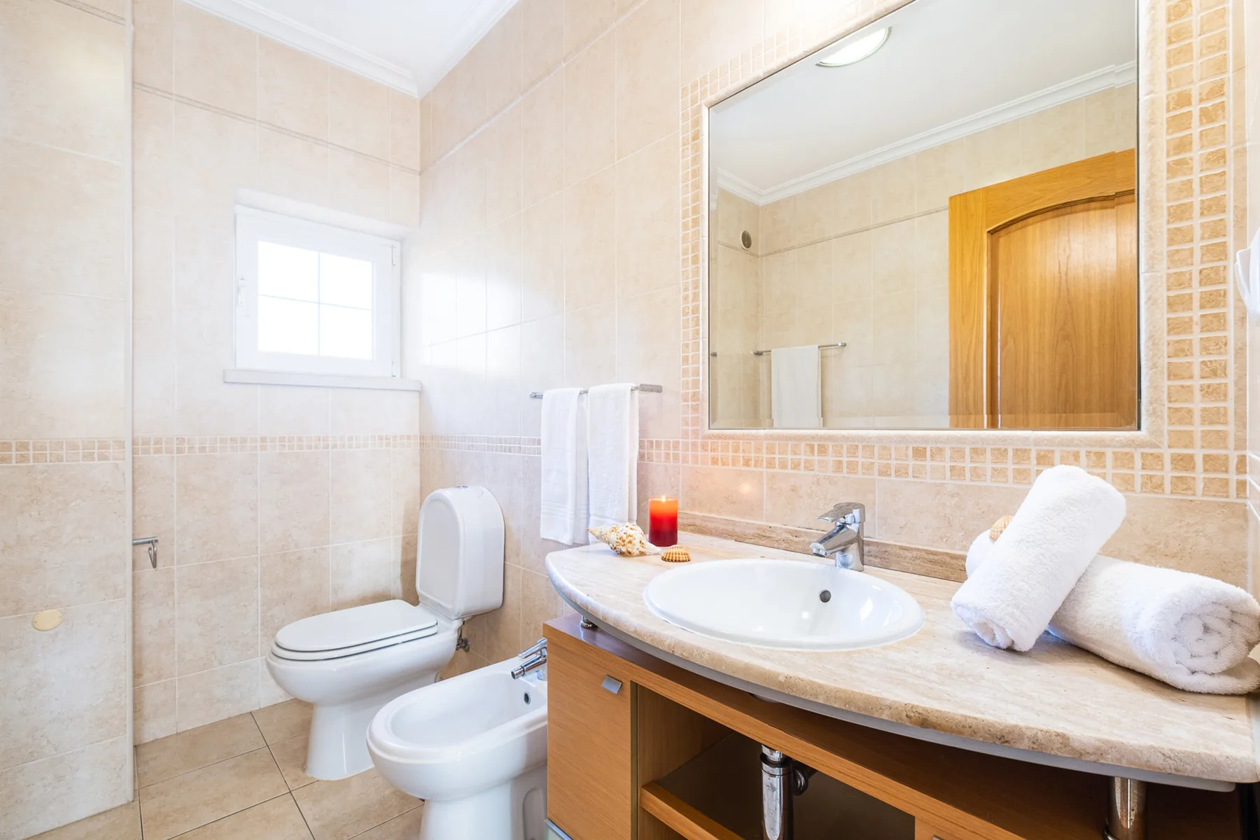 Un baño alicatado con lavabo, inodoro, bidé y un gran espejo de pared.