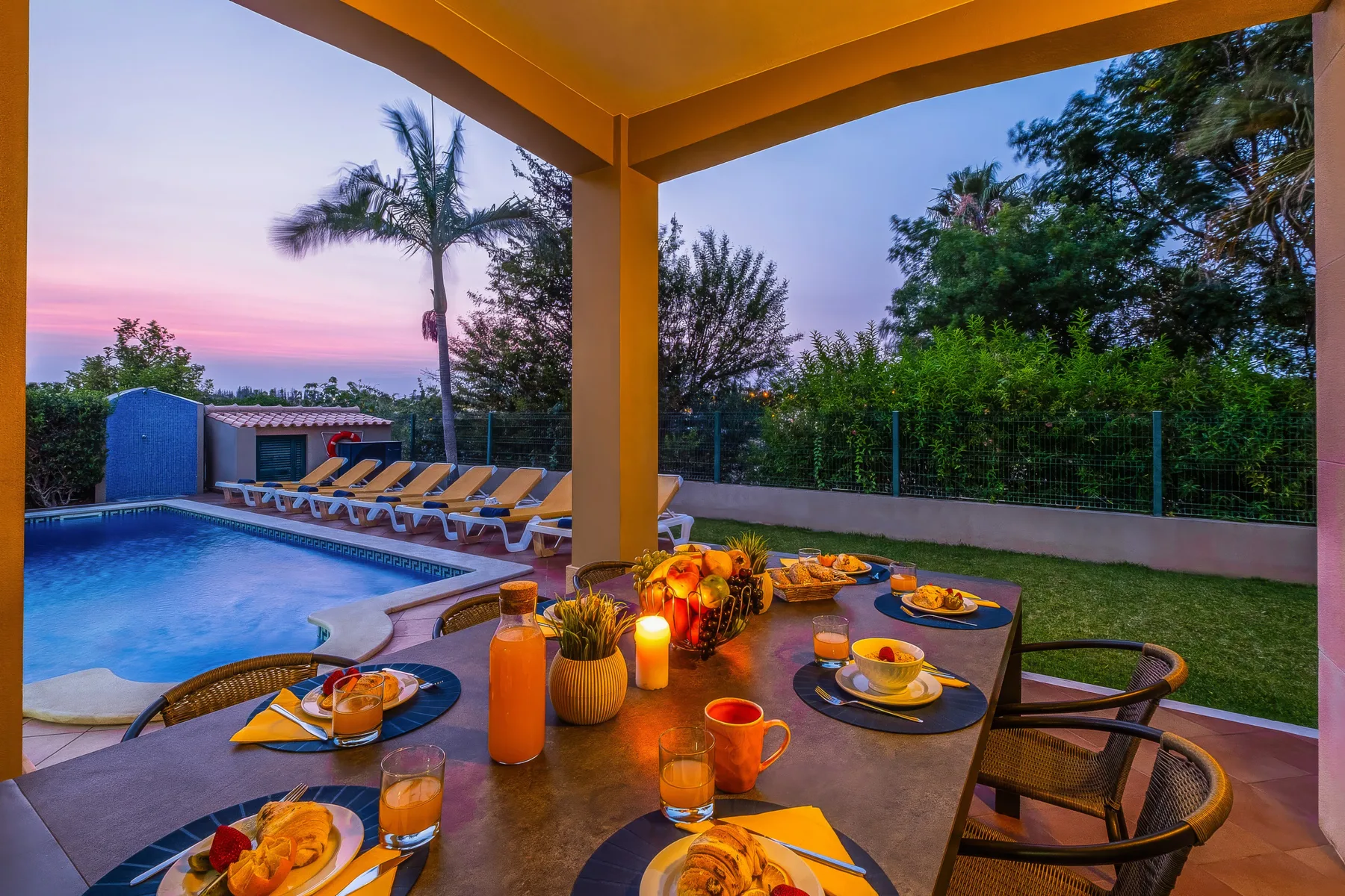Una mesa de comedor al aire libre junto a una piscina al atardecer.