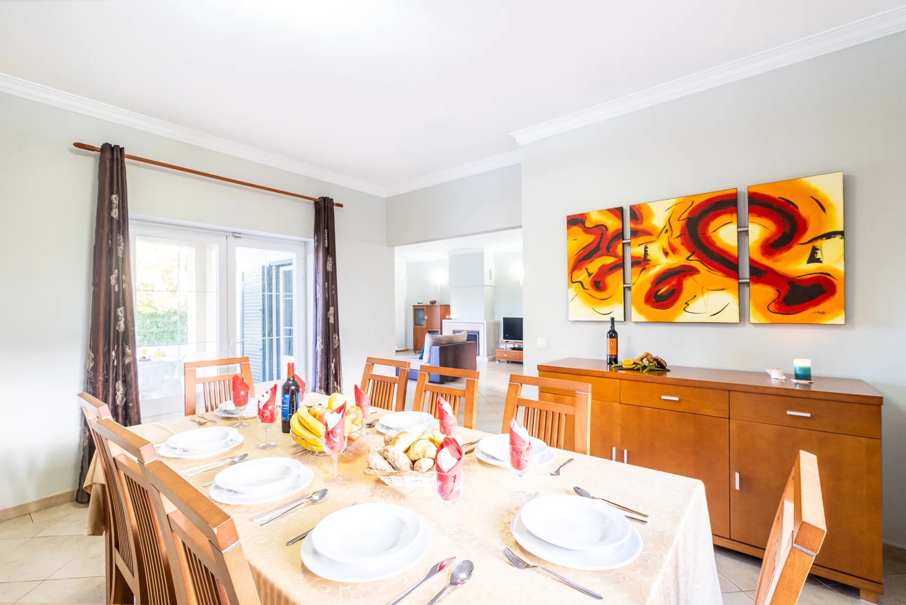 Comedor con la mesa puesta y arte abstracto colorido sobre un aparador de madera.