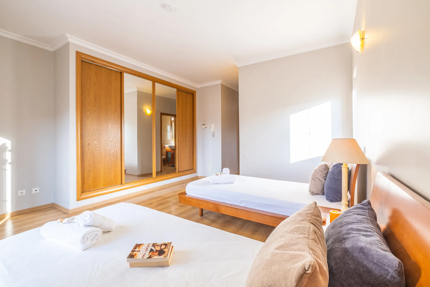 Un dormitorio luminoso con dos camas y un armario de madera con espejo.
