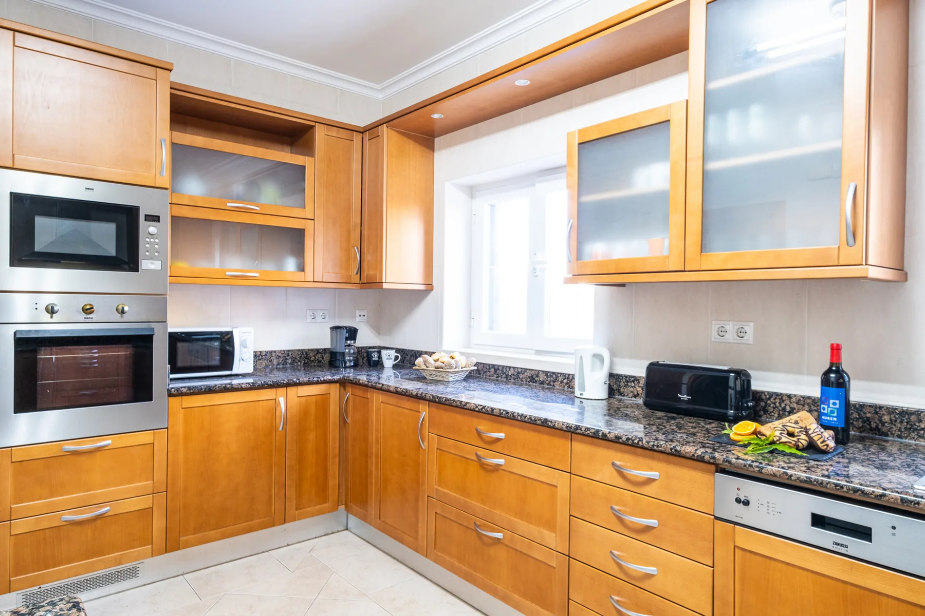 Una cocina luminosa con armarios de madera, encimeras oscuras y electrodomésticos integrados.