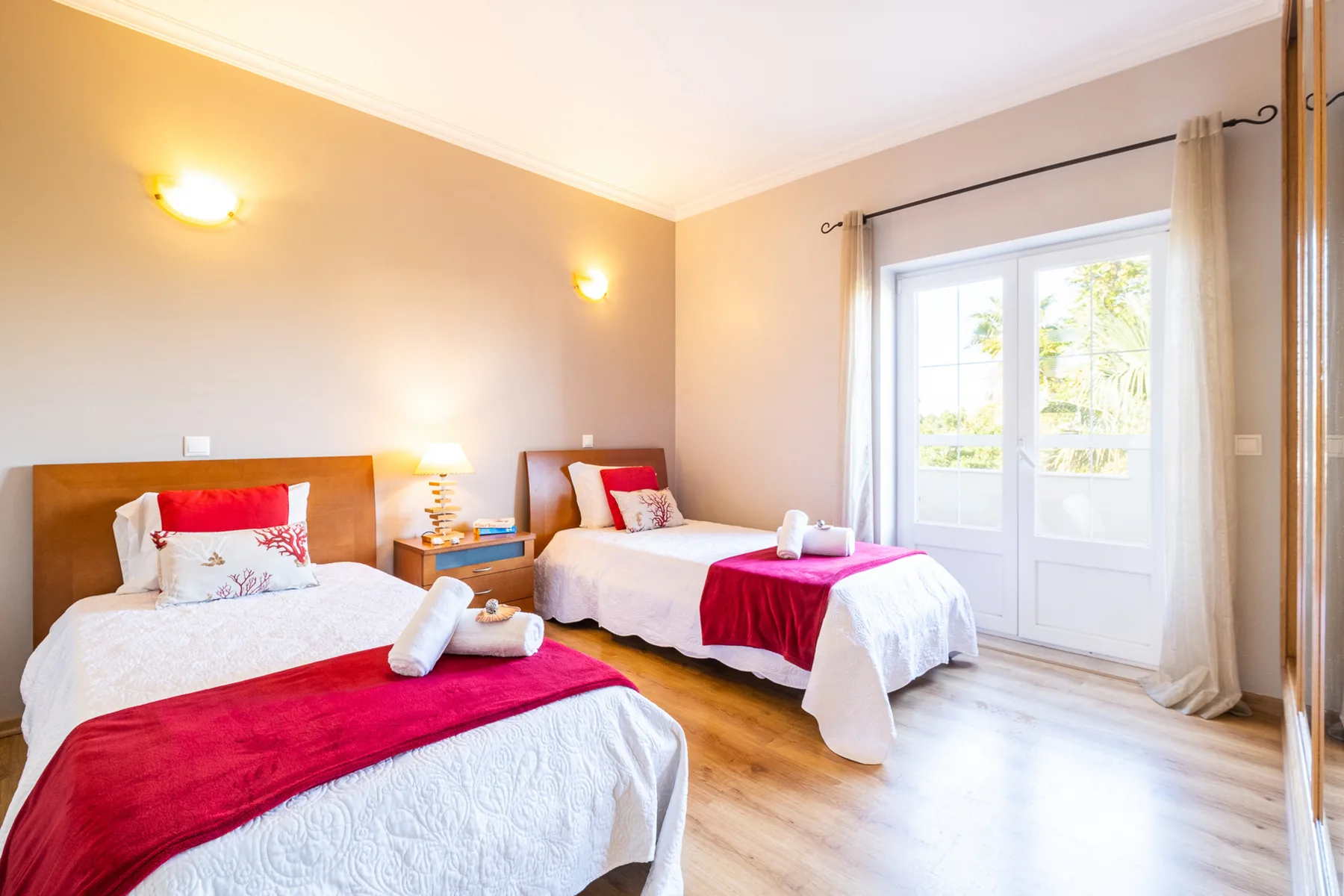 Un dormitorio luminoso con dos camas vestidas de blanco y detalles rojos.