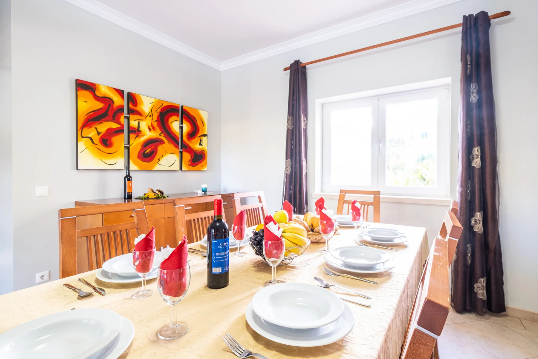 Un comedor con la mesa puesta con platos y copas junto a una ventana luminosa.