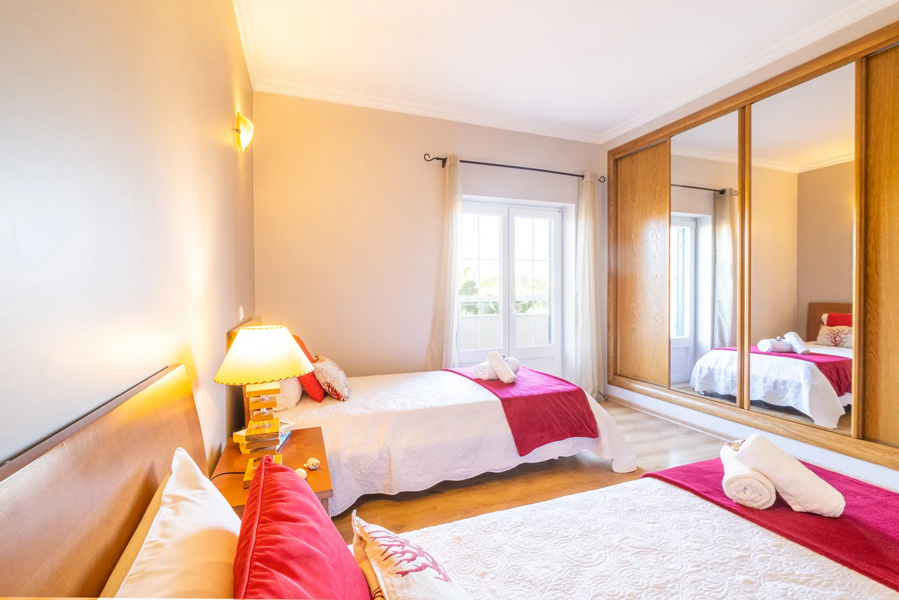 Un dormitorio luminoso con camas, una lámpara de mesilla y puertas de armario con espejo.