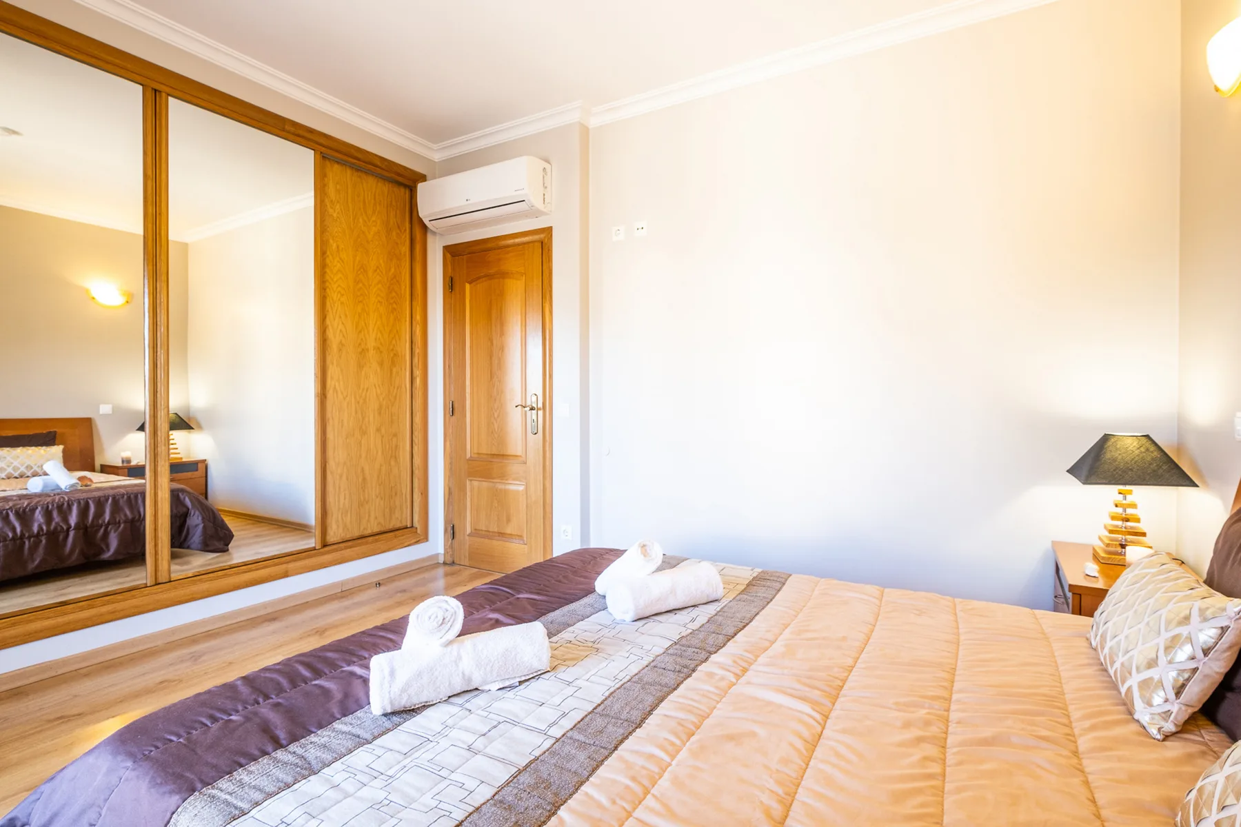 Un dormitorio con una cama, un armario con espejo y una puerta de madera.