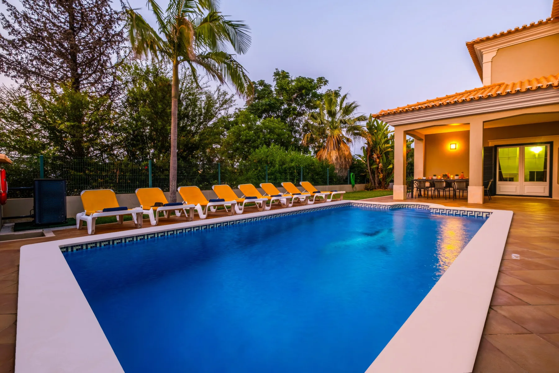 Una piscina junto a un patio con asientos y una terraza cubierta.