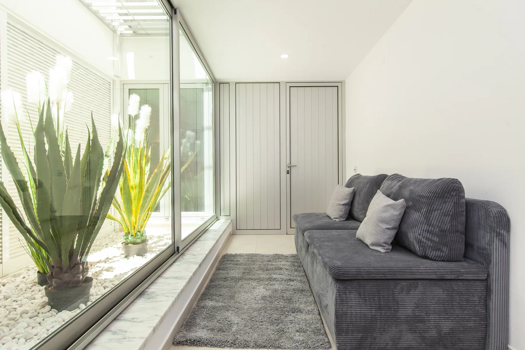 Una luminosa zona de estar con asientos grises junto a una pared de vidrio y plantas.