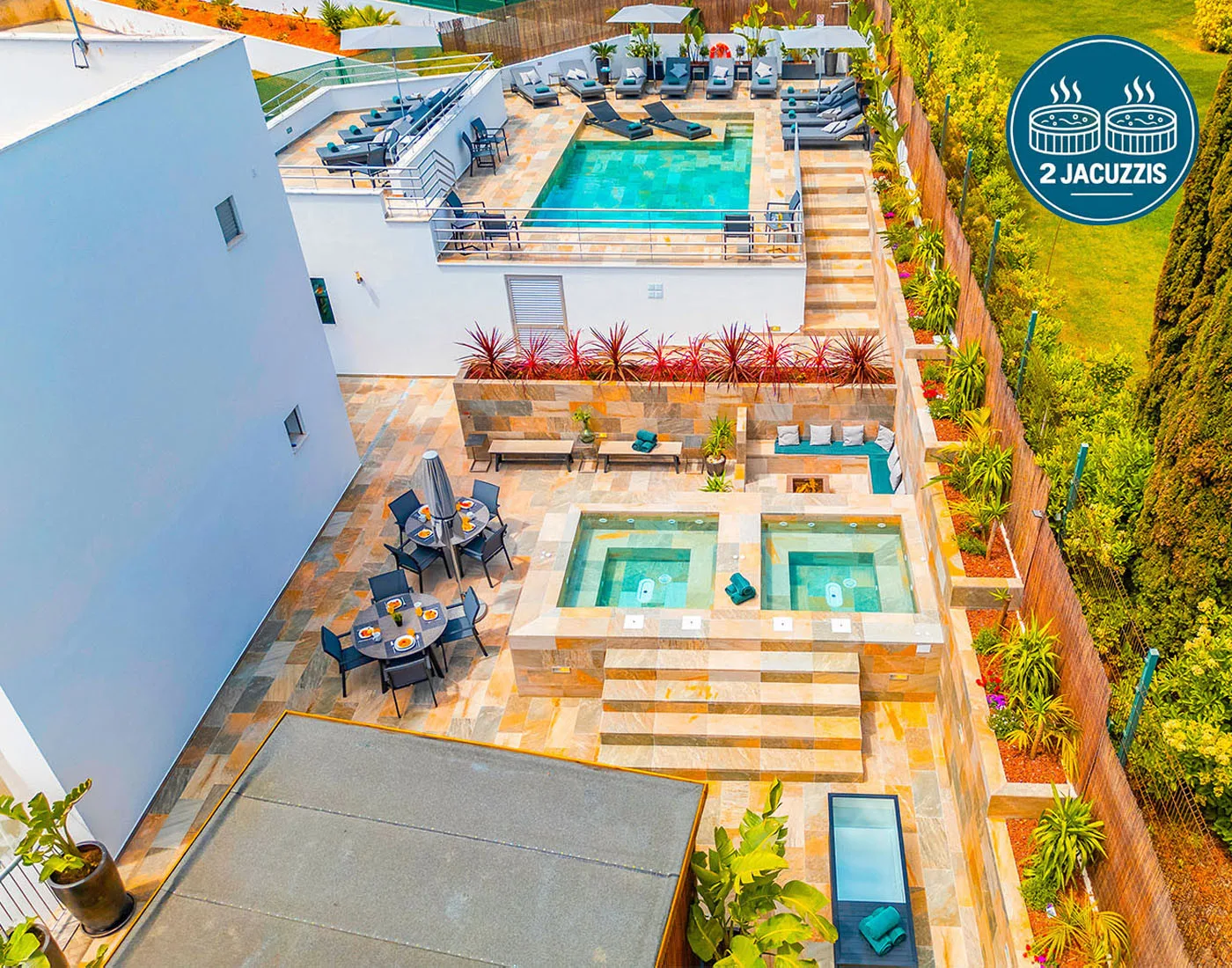 Una terraza exterior con piscina de agua turquesa, asientos y dos spas cuadrados.