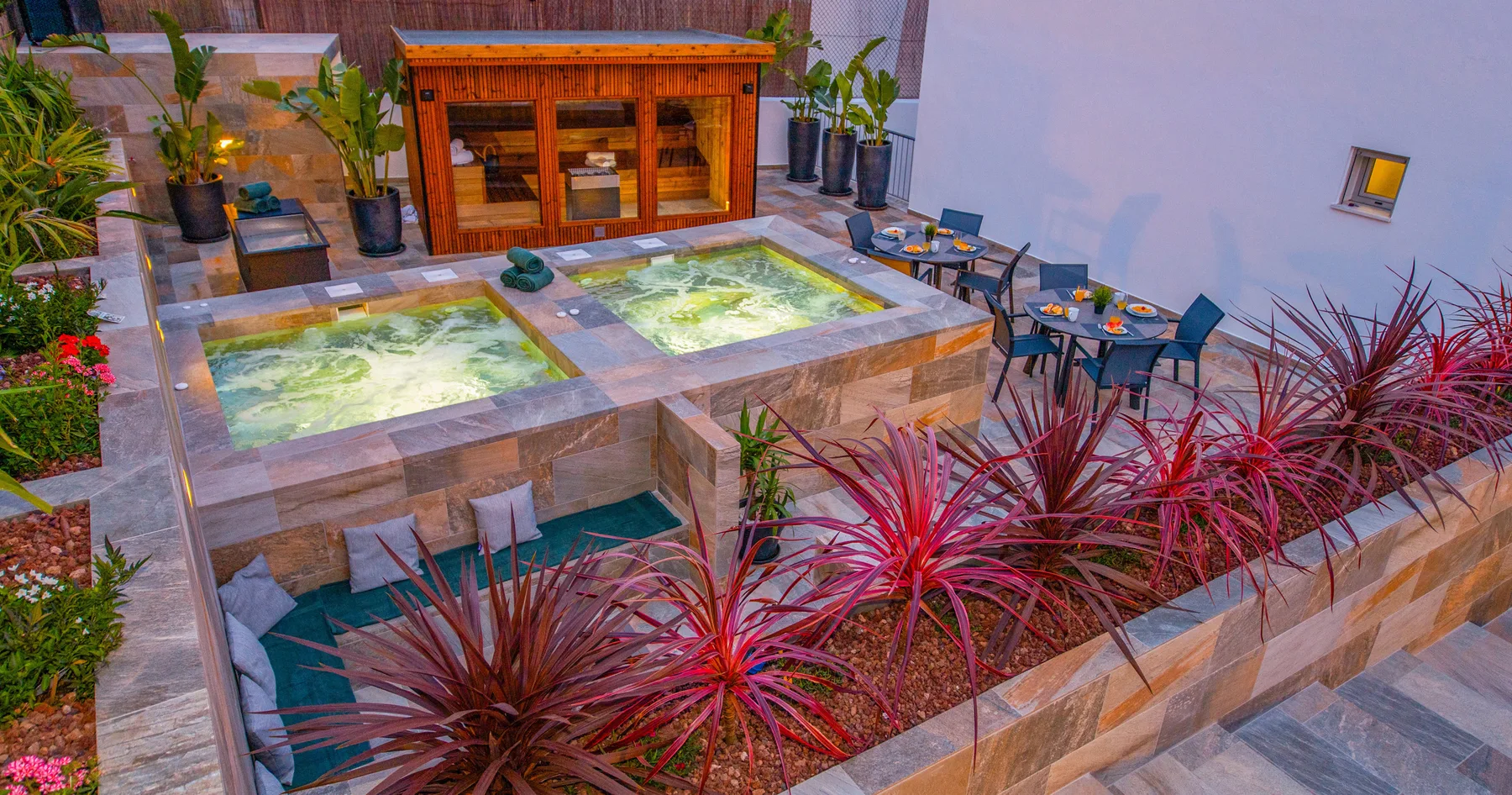 Patio al aire libre con dos jacuzzis iluminados, asientos y una barra de madera.