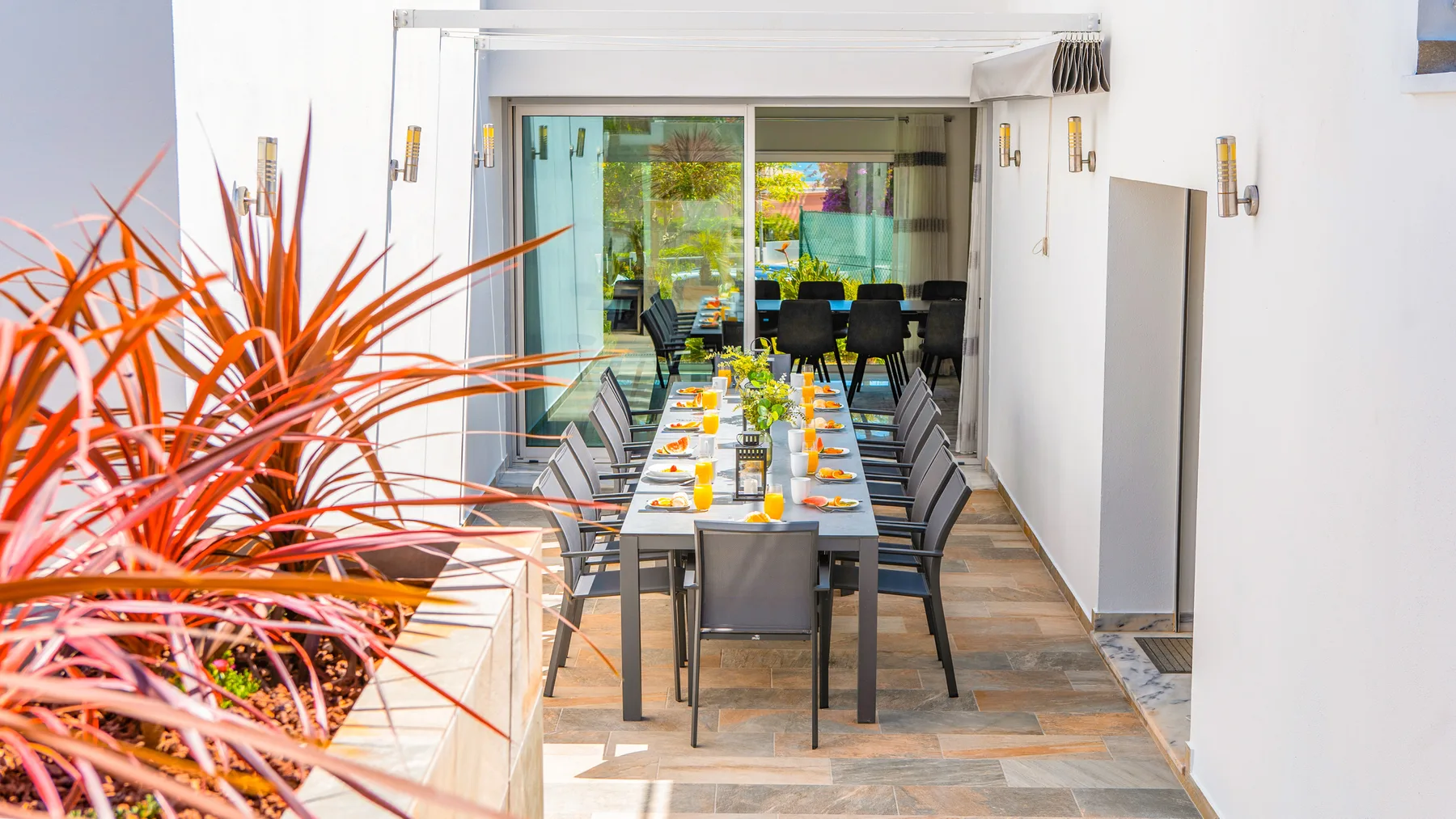 Comedor al aire libre con una mesa larga junto a puertas corredizas de vidrio.