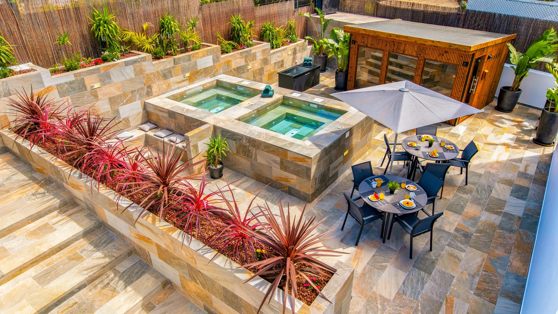 Un patio pavimentado cuenta con una piscina elevada rectangular, asientos al aire libre y una sombrilla.