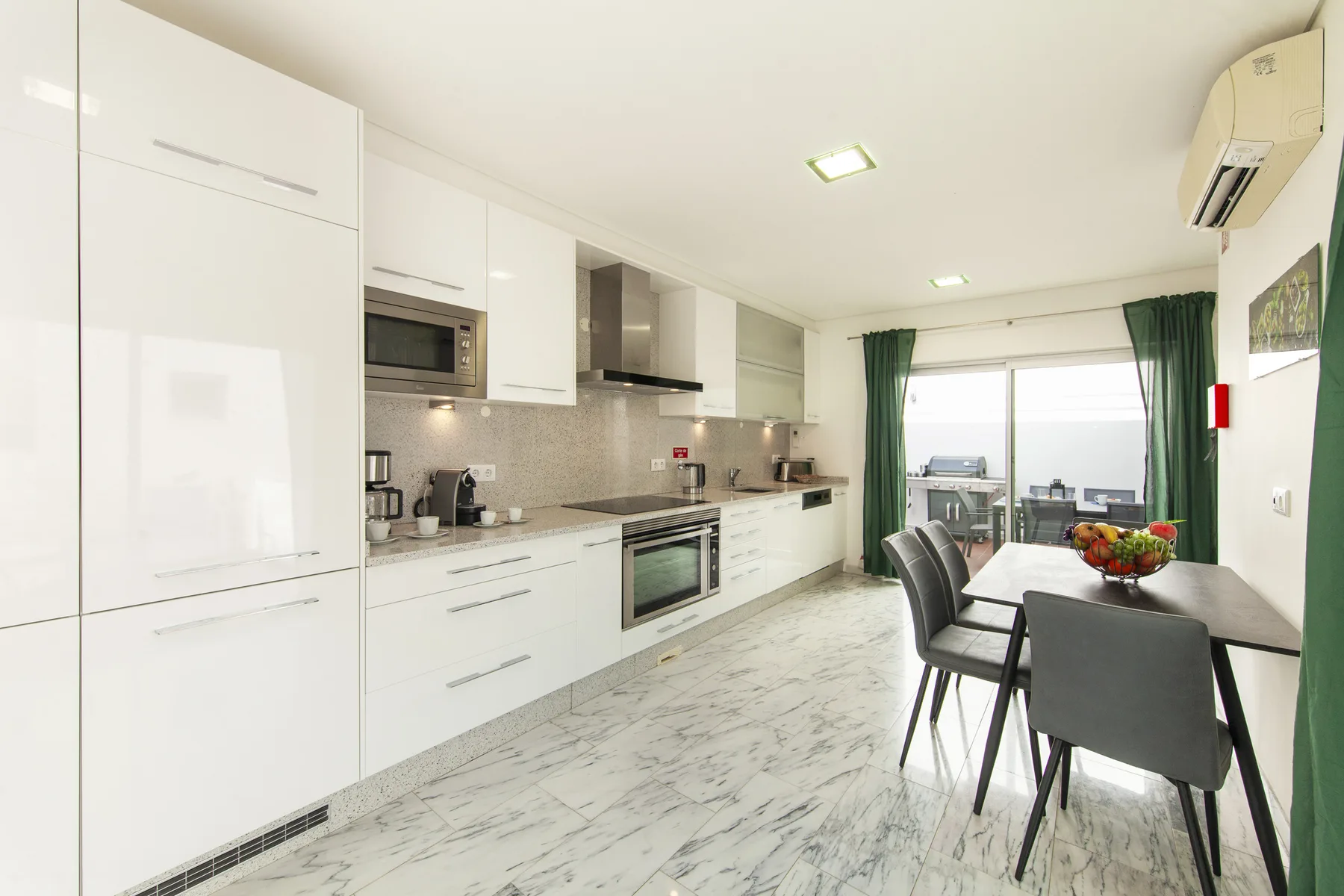 Una cocina y comedor luminosos con gabinetes blancos y una mesa junto a la ventana.