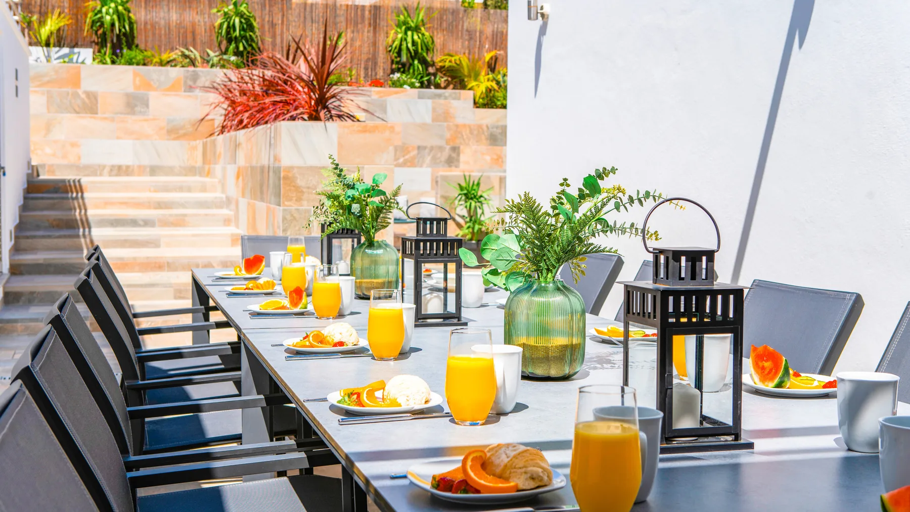 Una mesa de comedor al aire libre está preparada con platos, bebidas y faroles decorativos.