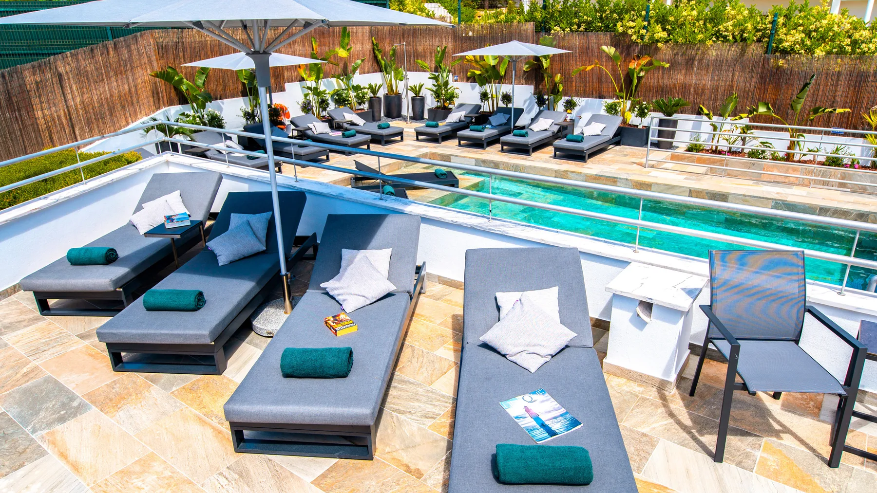 Una terraza soleada junto a la piscina tiene asientos reclinables y sombrillas.