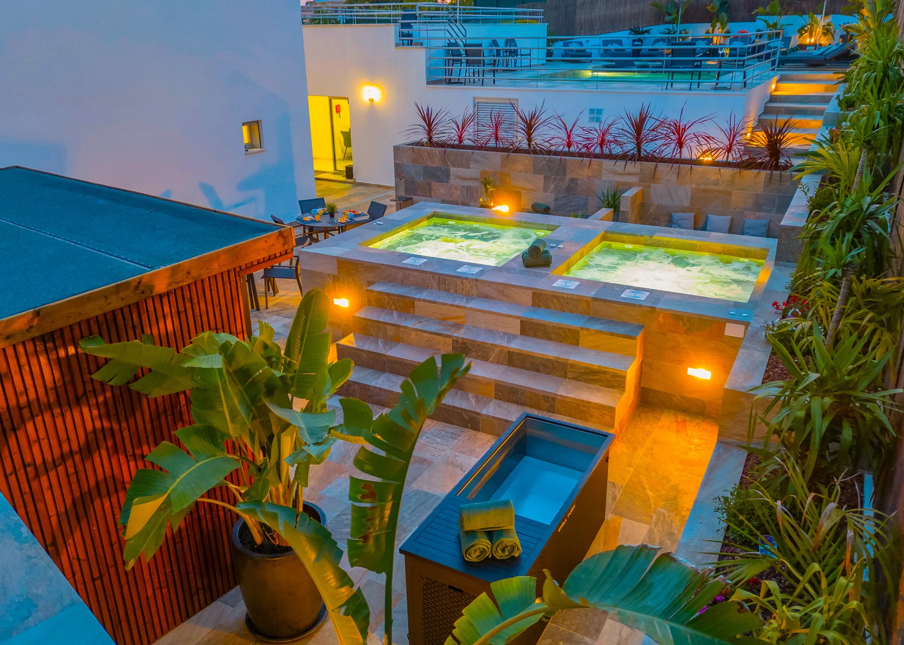 Una zona de spa exterior iluminada cuenta con dos jacuzzis y una piscina pequeña.
