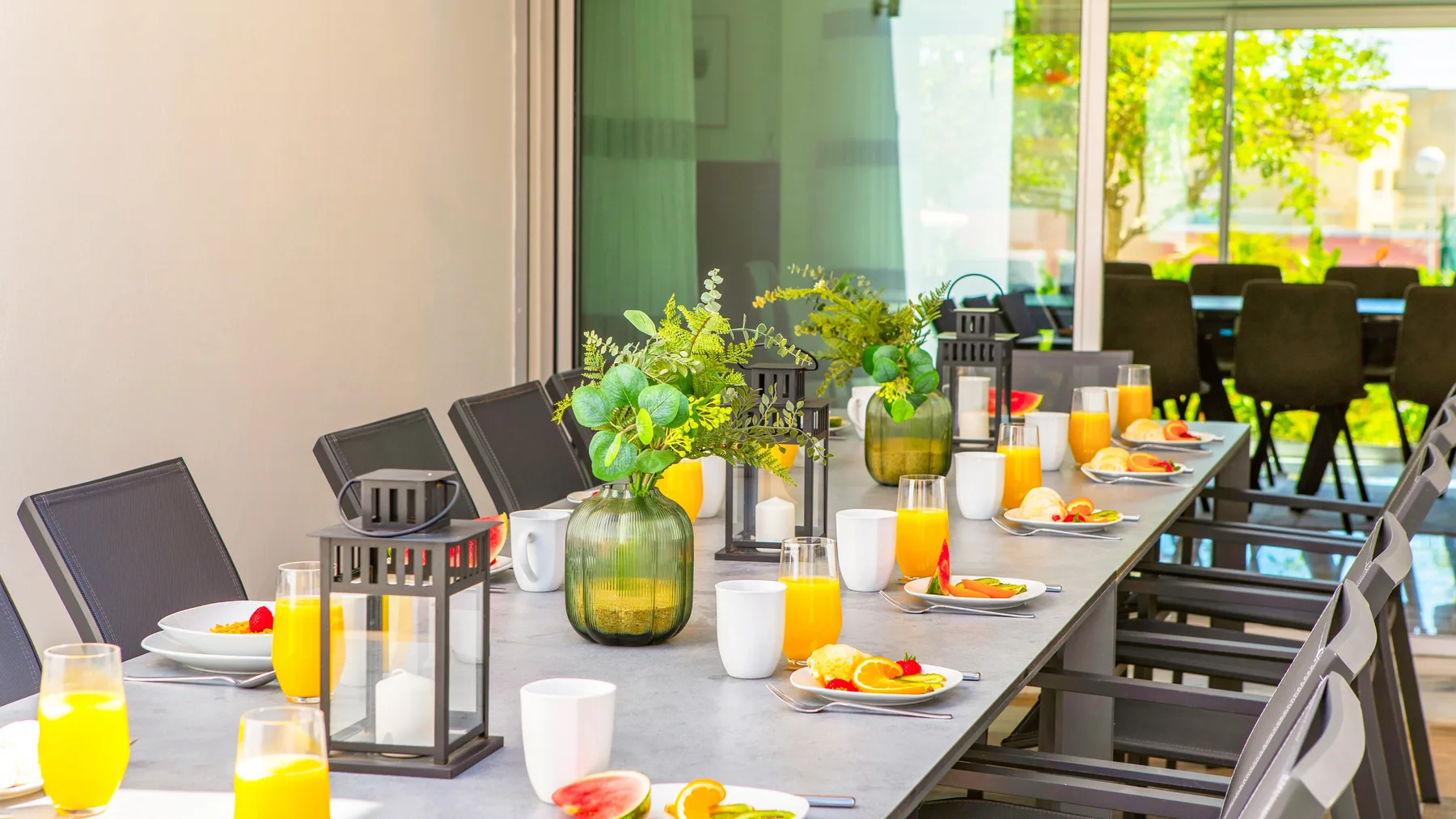Una mesa de comedor está dispuesta con platos y bebidas junto a una fila de sillas.