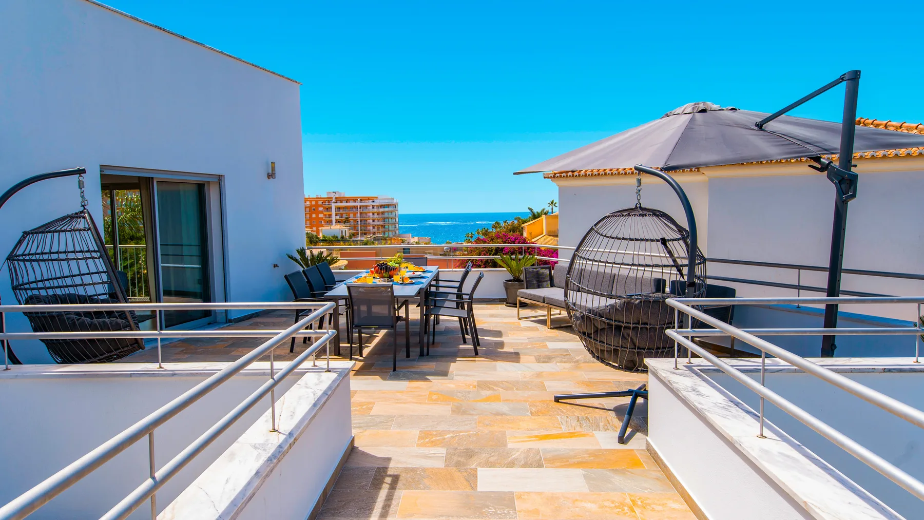 Una terraza en la azotea con asientos al aire libre y sillas colgantes da al mar.