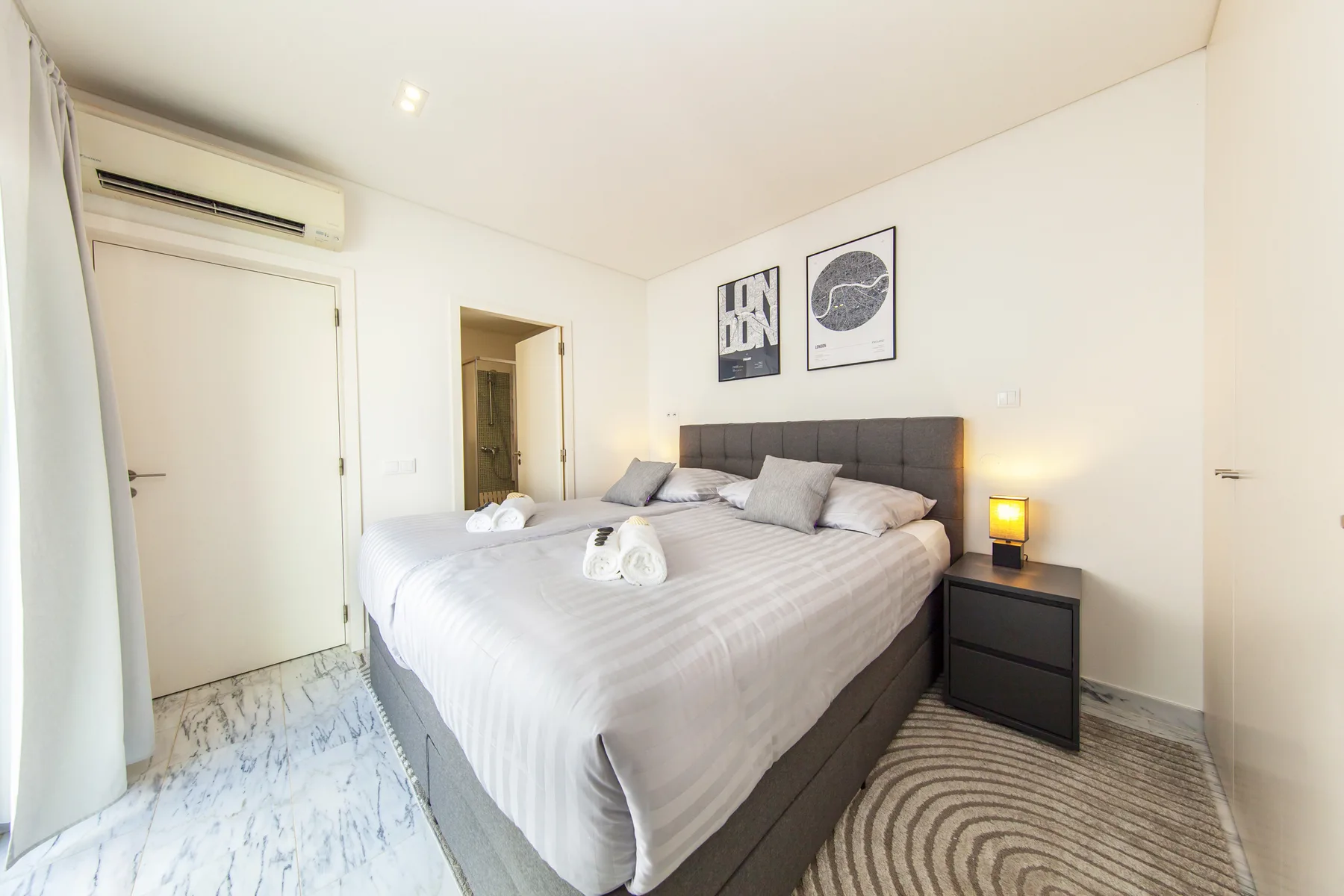 Un dormitorio luminoso con una cama grande y cuadros enmarcados sobre el cabecero.