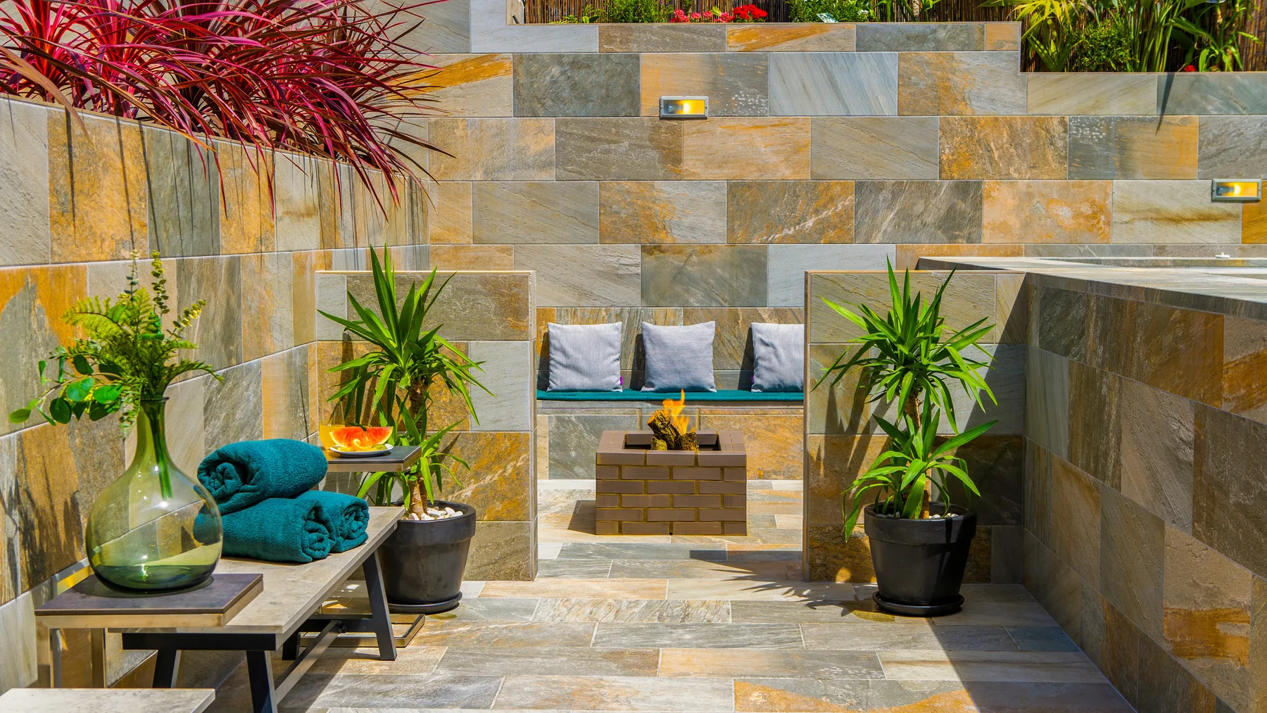 Un patio exterior con banco integrado, plantas en macetas y una mesa baja.