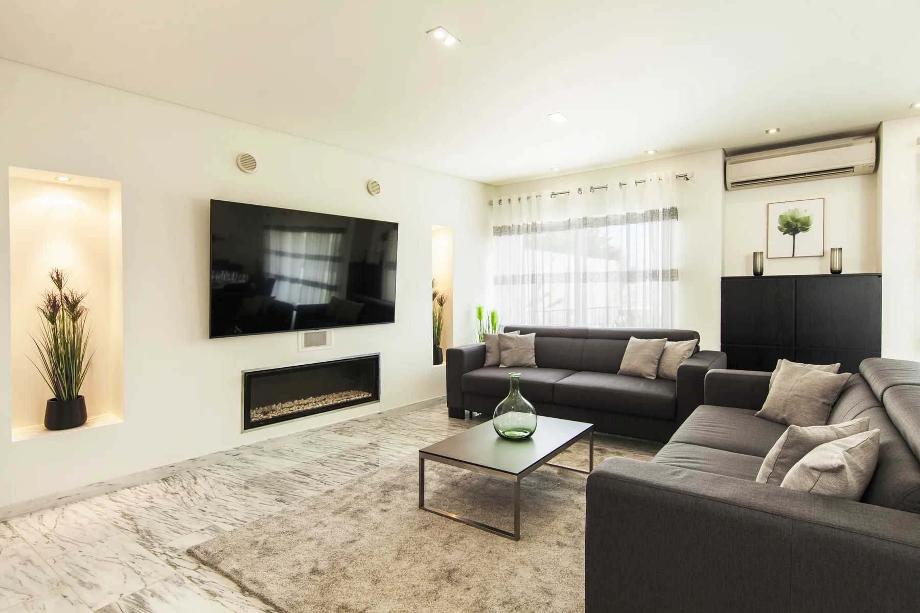 Una sala luminosa con asientos oscuros, una mesa de centro y un televisor en la pared.