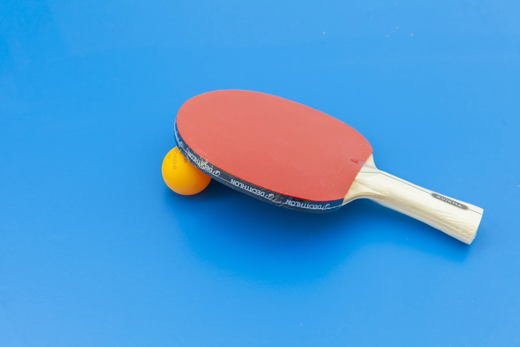 Una pala de tenis de mesa y una pelota están sobre una superficie azul.