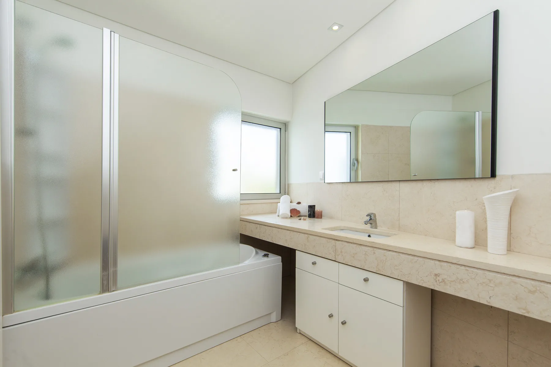 Un baño luminoso con bañera, mampara de vidrio esmerilado y un tocador largo.