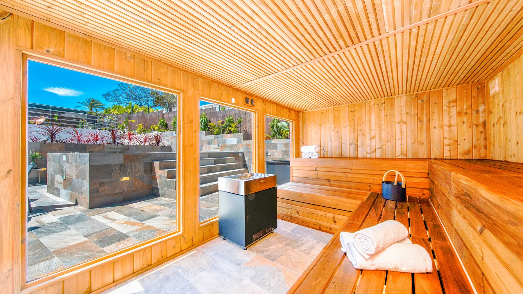 Una sauna revestida de madera tiene asientos en niveles y vistas por grandes ventanas.