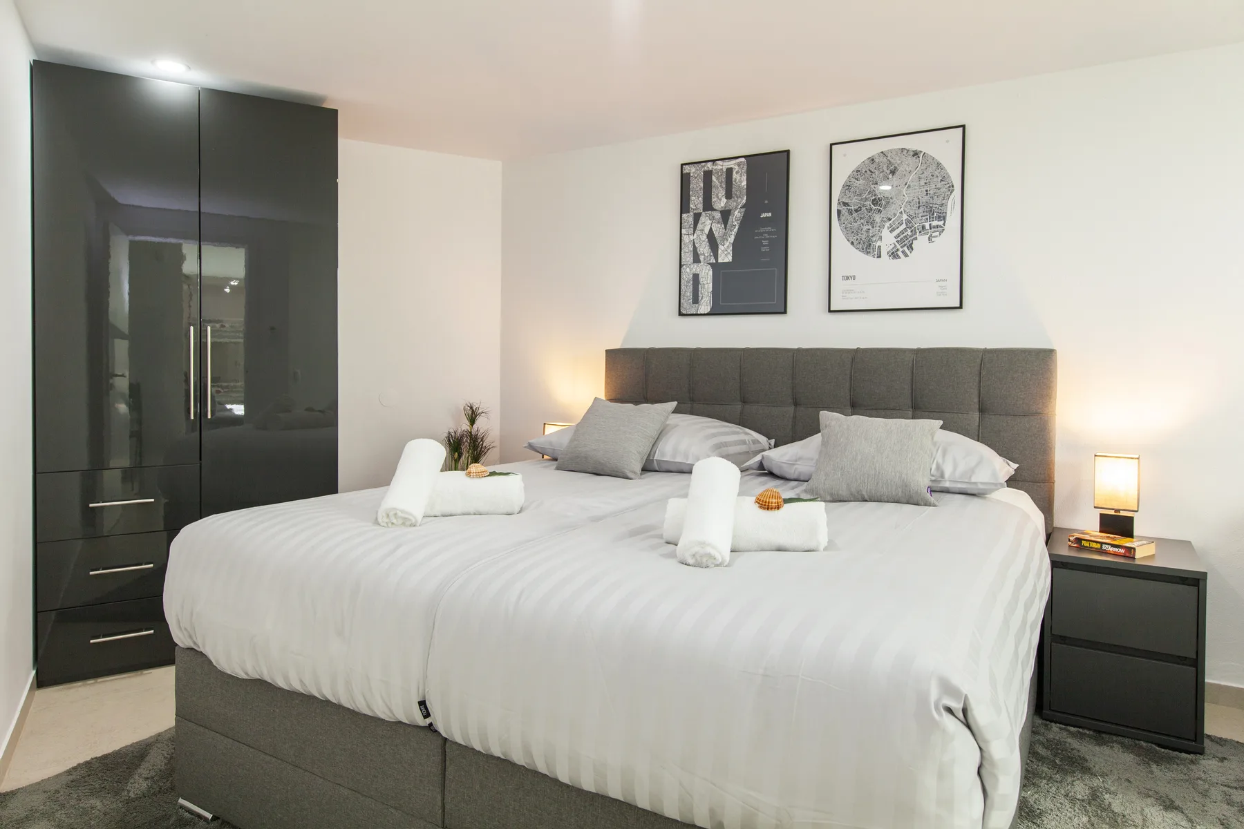 Un dormitorio con una cama grande, cabecero tapizado gris y armario oscuro.