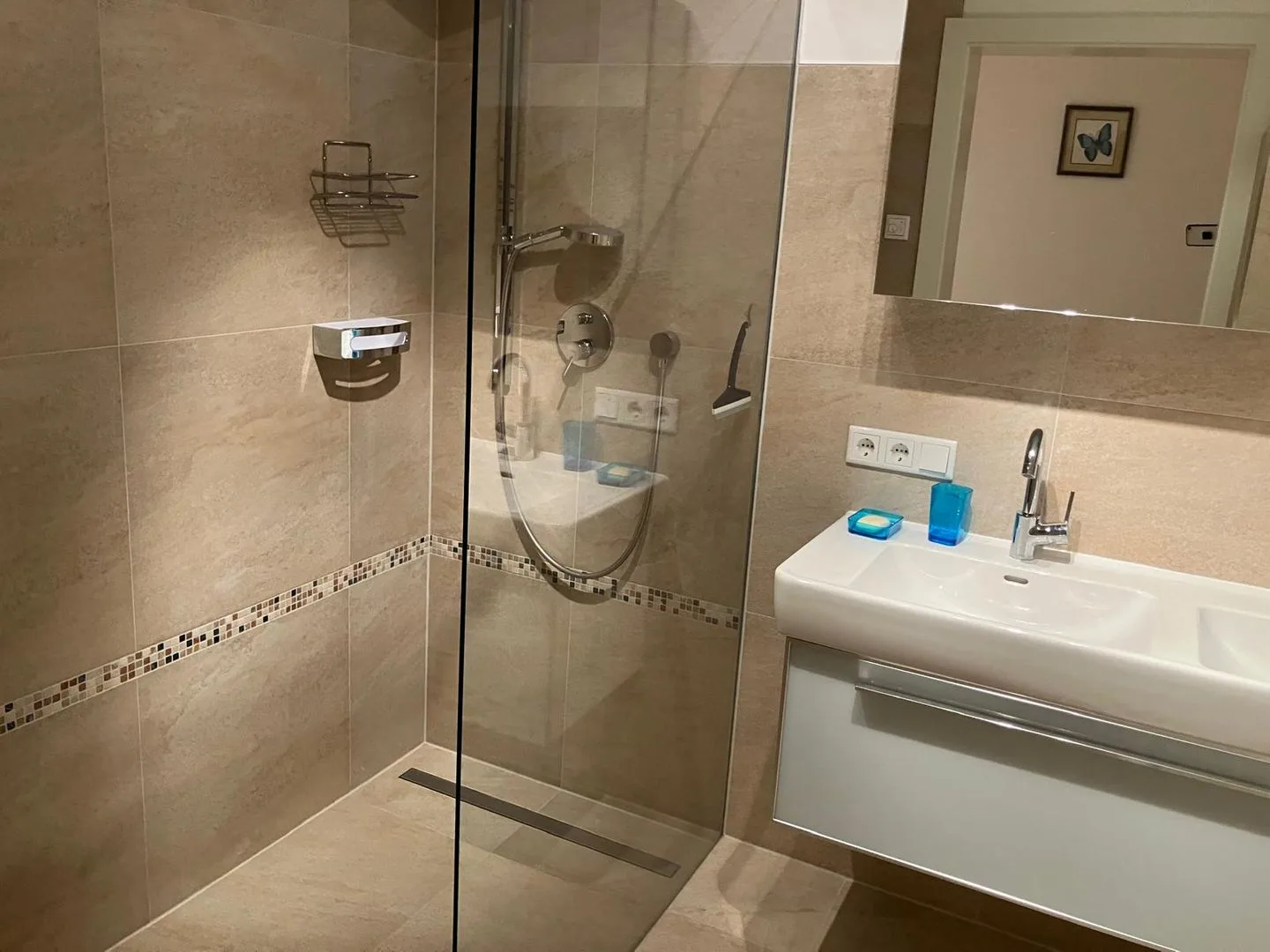 Un baño con azulejos, una ducha de vidrio y un lavabo bajo un espejo.