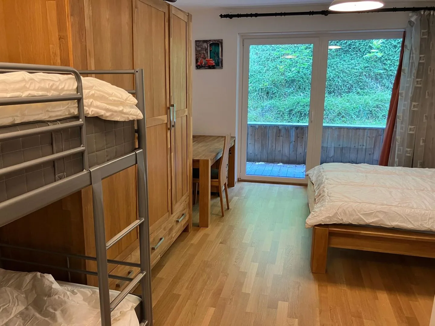 Un dormitorio con literas, una cama de madera y puertas de vidrio frente a la vegetación.