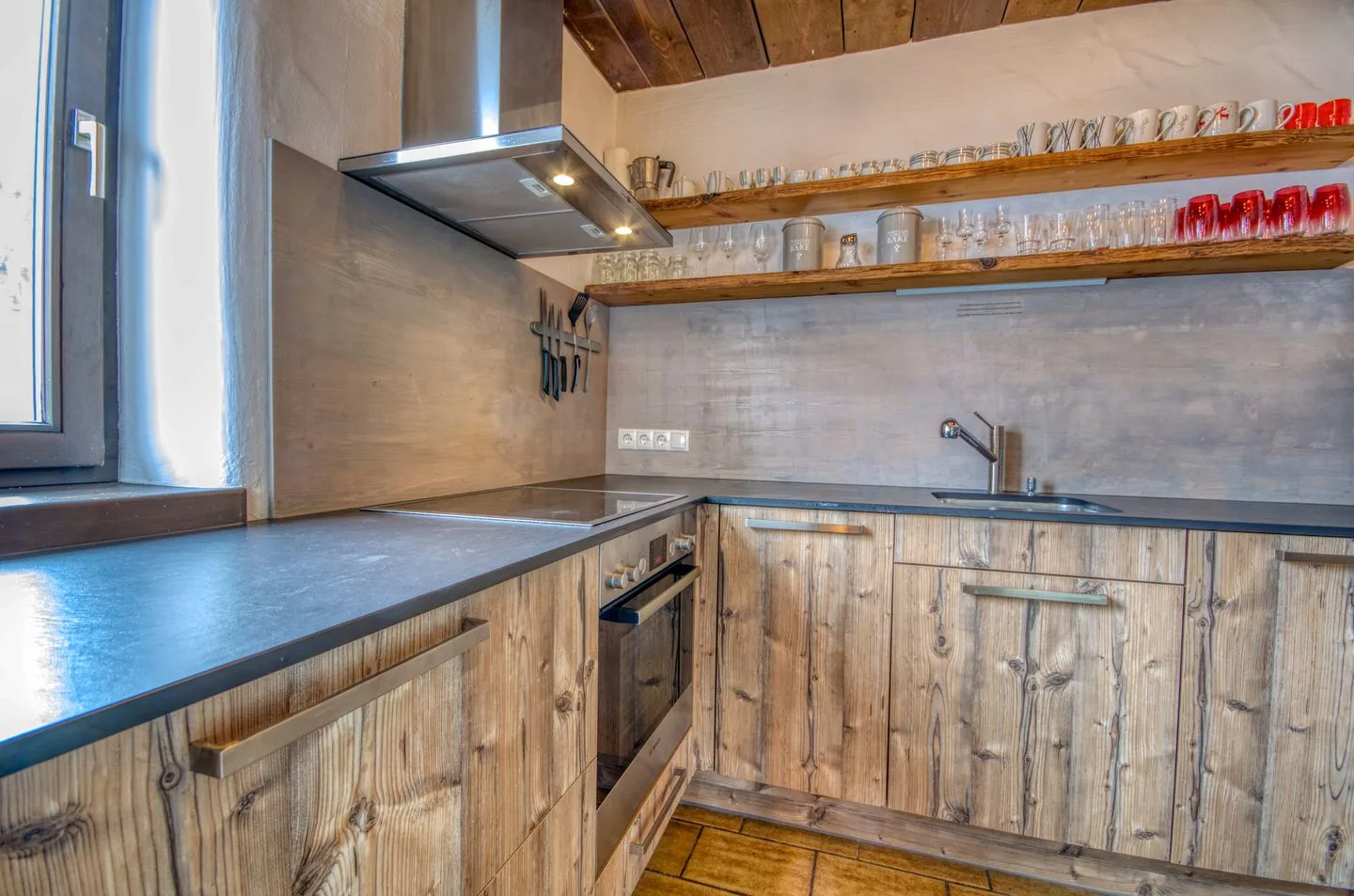Una cocina con gabinetes de madera, encimeras oscuras y estantes abiertos con cristalería.