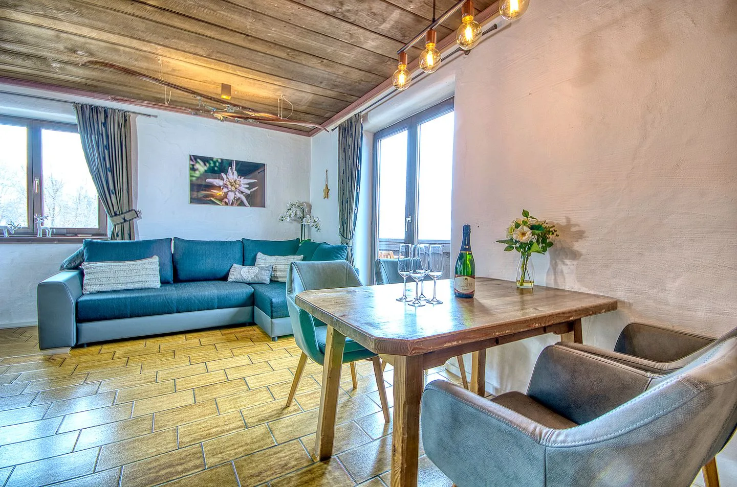 Una sala de estar y comedor con asientos azules, una mesa de madera y grandes ventanas.