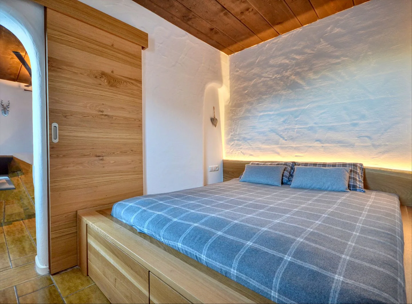 Un dormitorio con una cama doble bajo un techo de madera y una pared texturizada con luz suave.