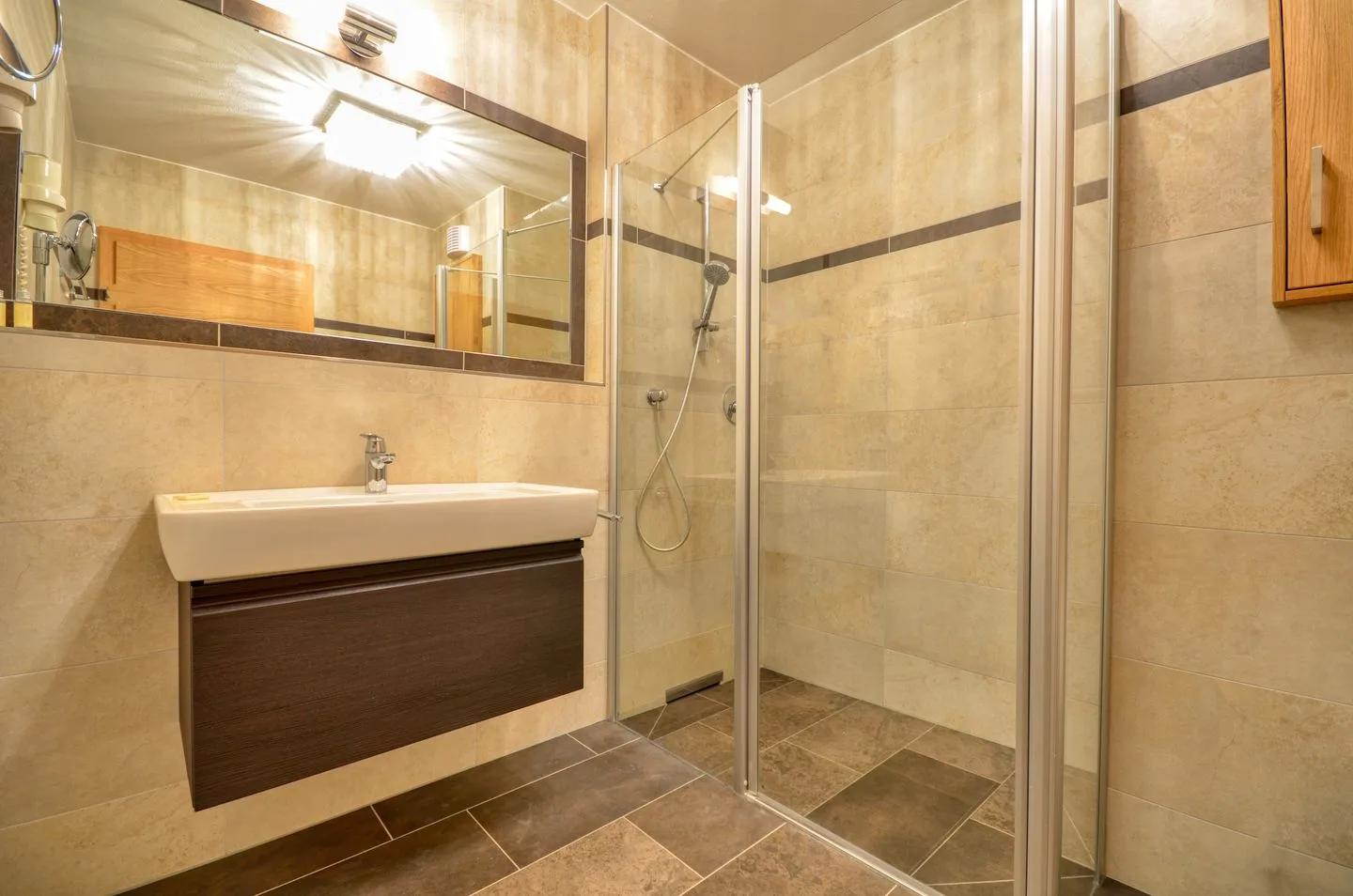 Un baño con azulejos, lavabo suspendido y ducha de vidrio.