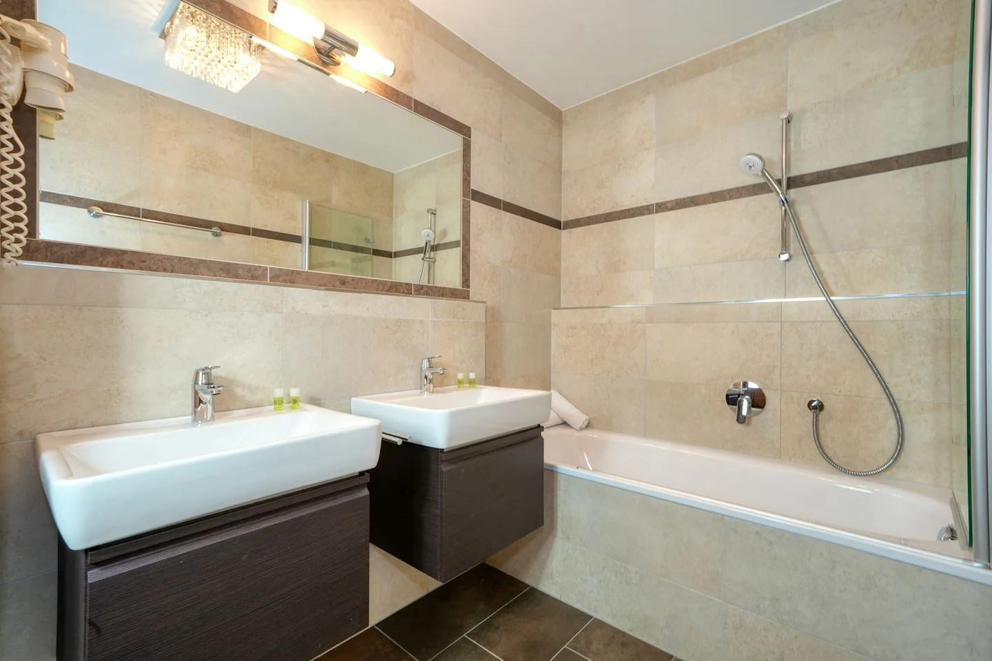 Un baño alicatado con bañera, ducha de mano y dos lavabos.