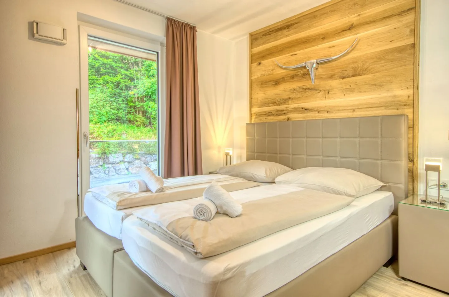Un dormitorio con una cama grande, ropa de cama neutra y una pared revestida de madera.