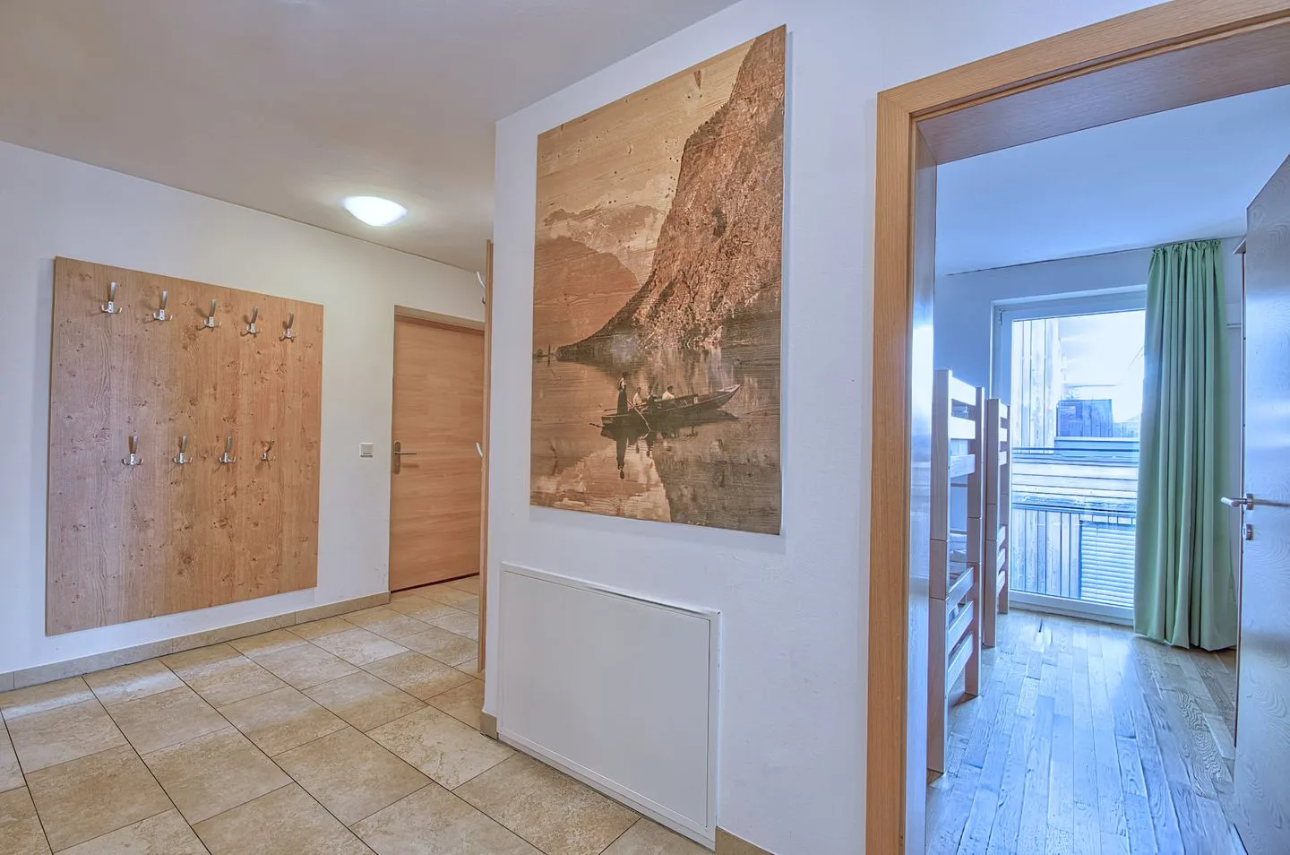 Un pasillo de baldosas con un perchero de madera y una puerta abierta a una habitación luminosa.