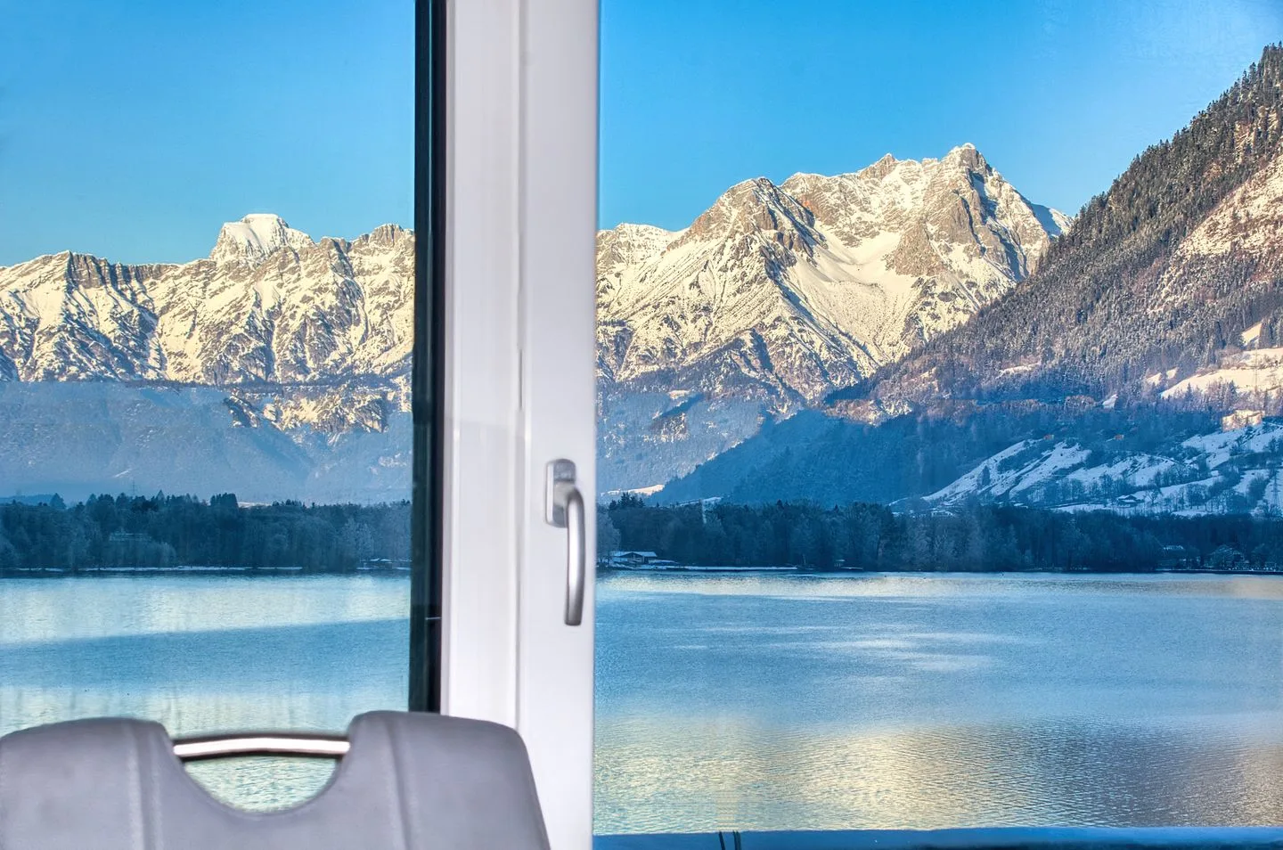 Un lago de montaña y picos nevados se ven a través de una ventana.