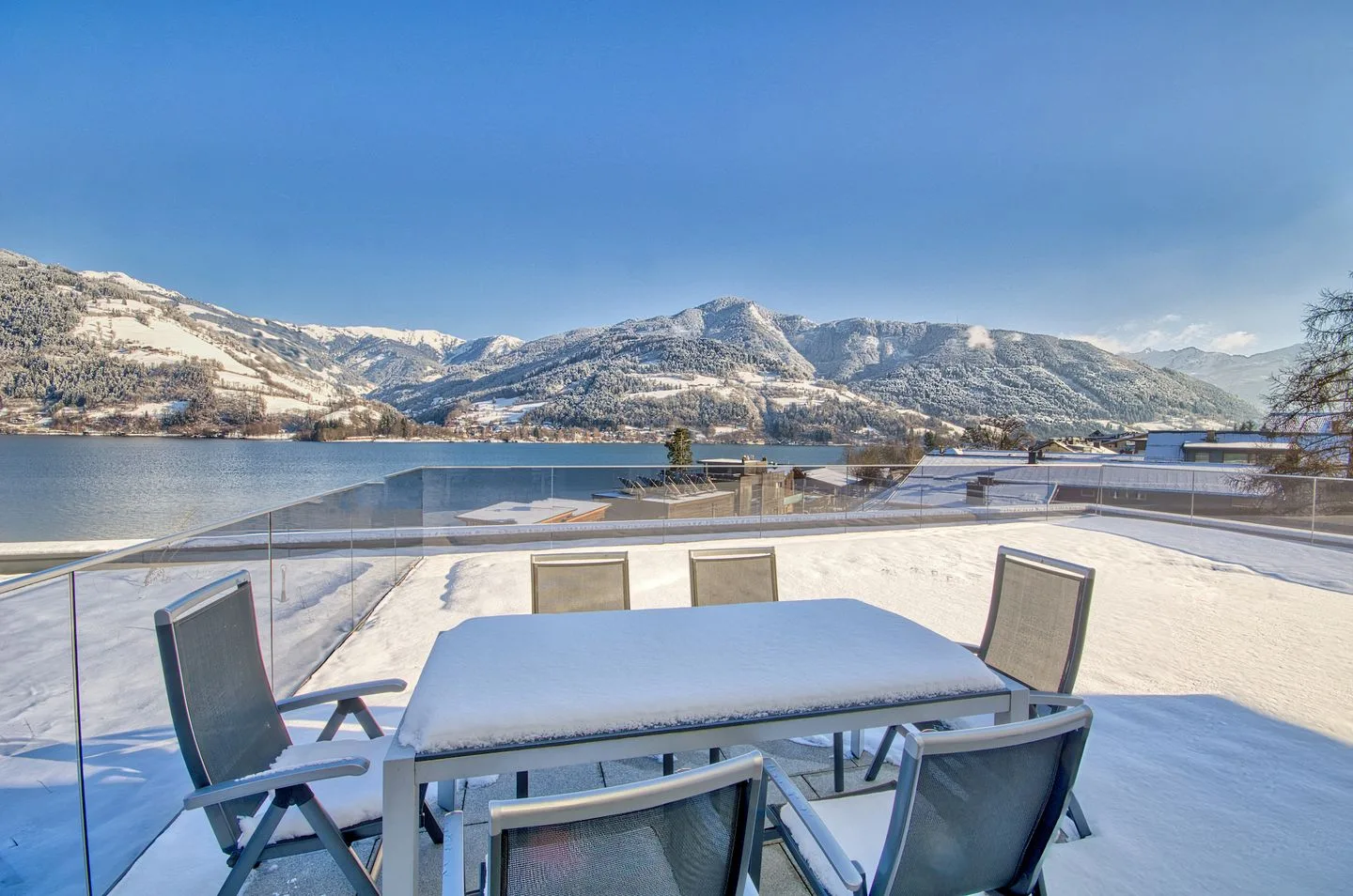 Una zona de comedor al aire libre da a un lago y montañas nevadas.