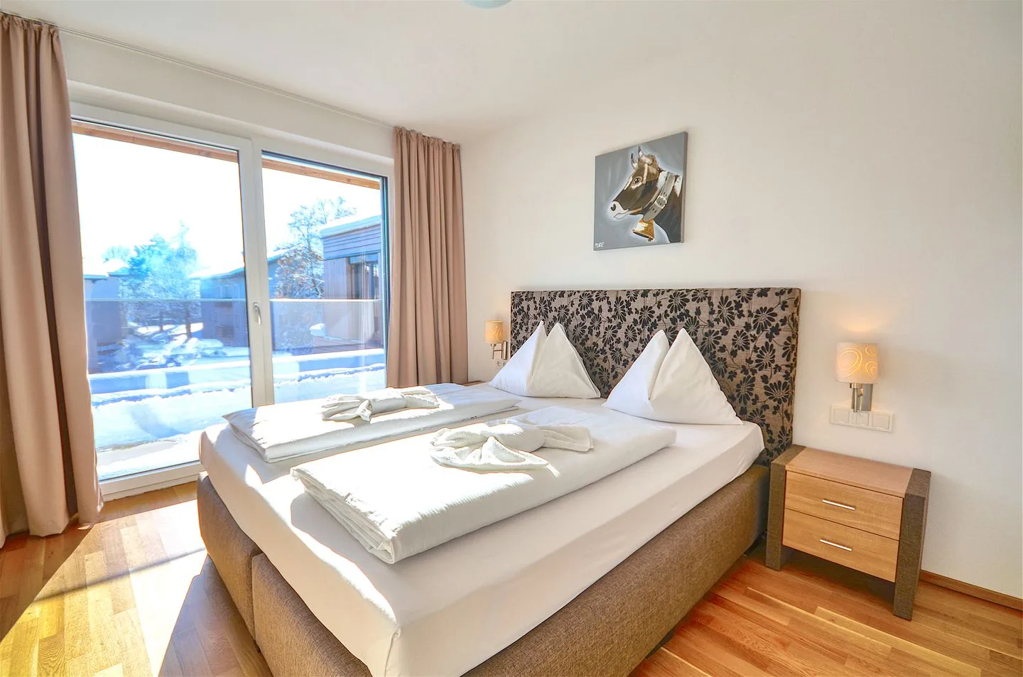 Un dormitorio con una cama doble junto a grandes ventanas y cortinas claras.
